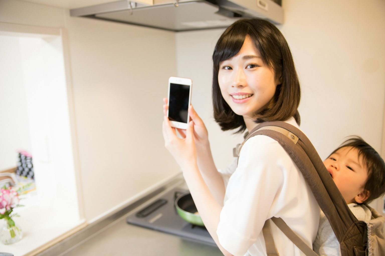 Mère tenant un smartphone dans la cuisine avec son enfant sur le dos