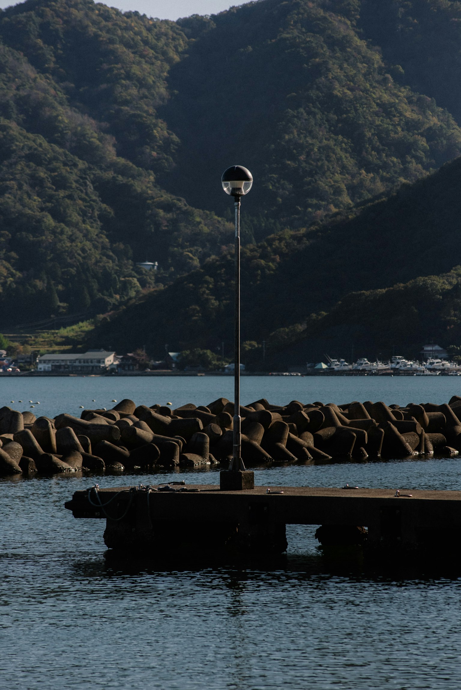 Steg im Wasser mit einem Leuchtturm und bergiger Landschaft
