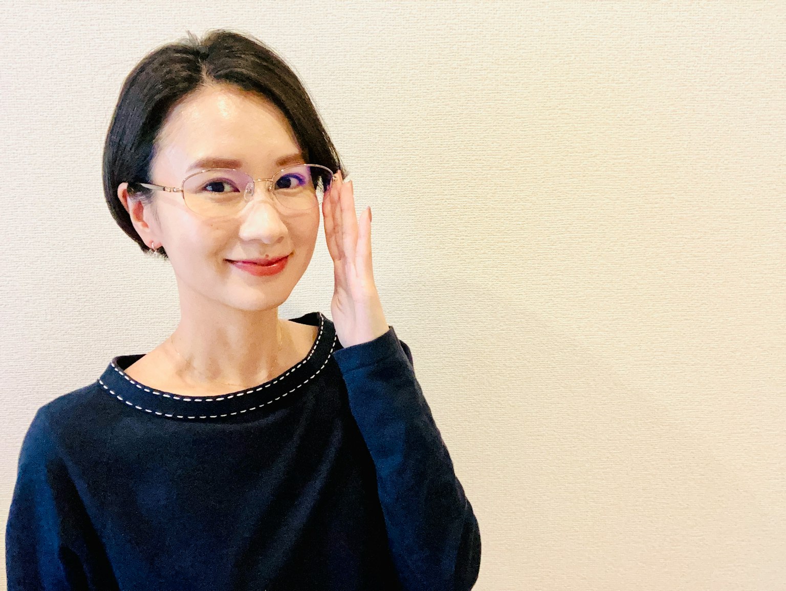 一位穿著黑色毛衣的女性正在調整眼鏡並微笑