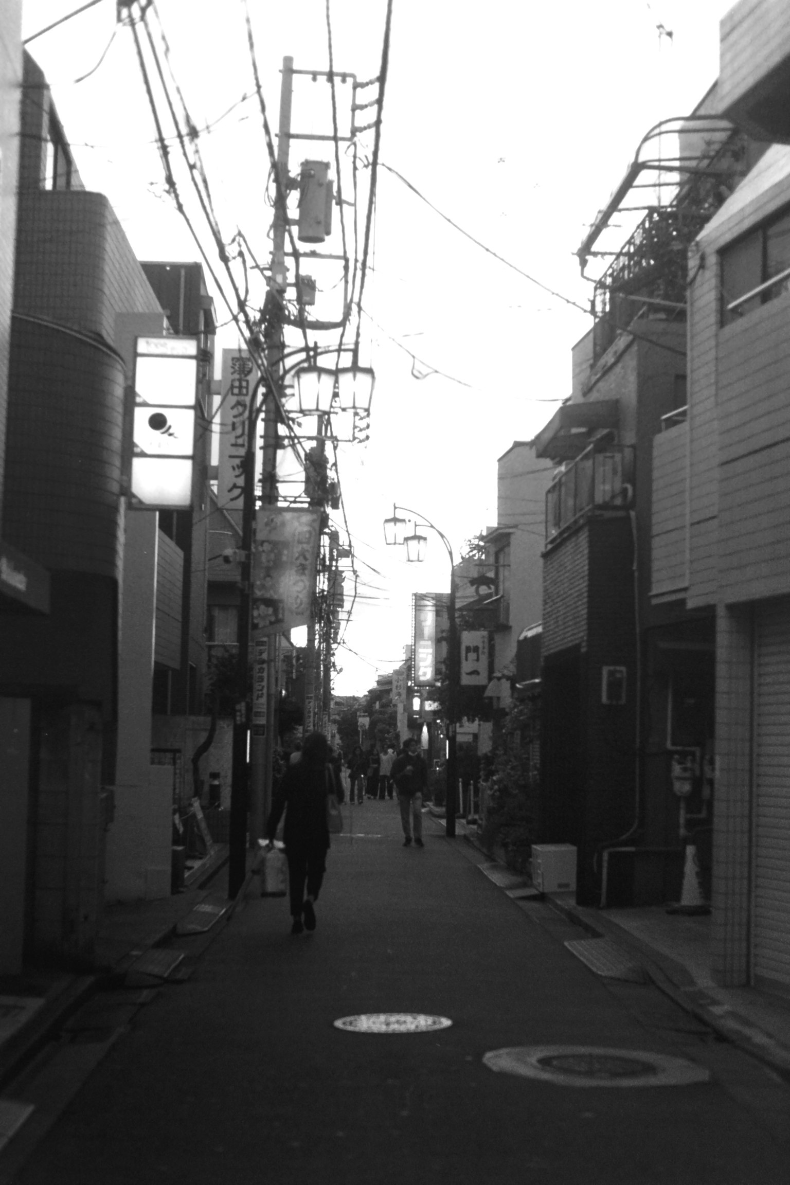 A person walking down a narrow black and white street with overhead power lines