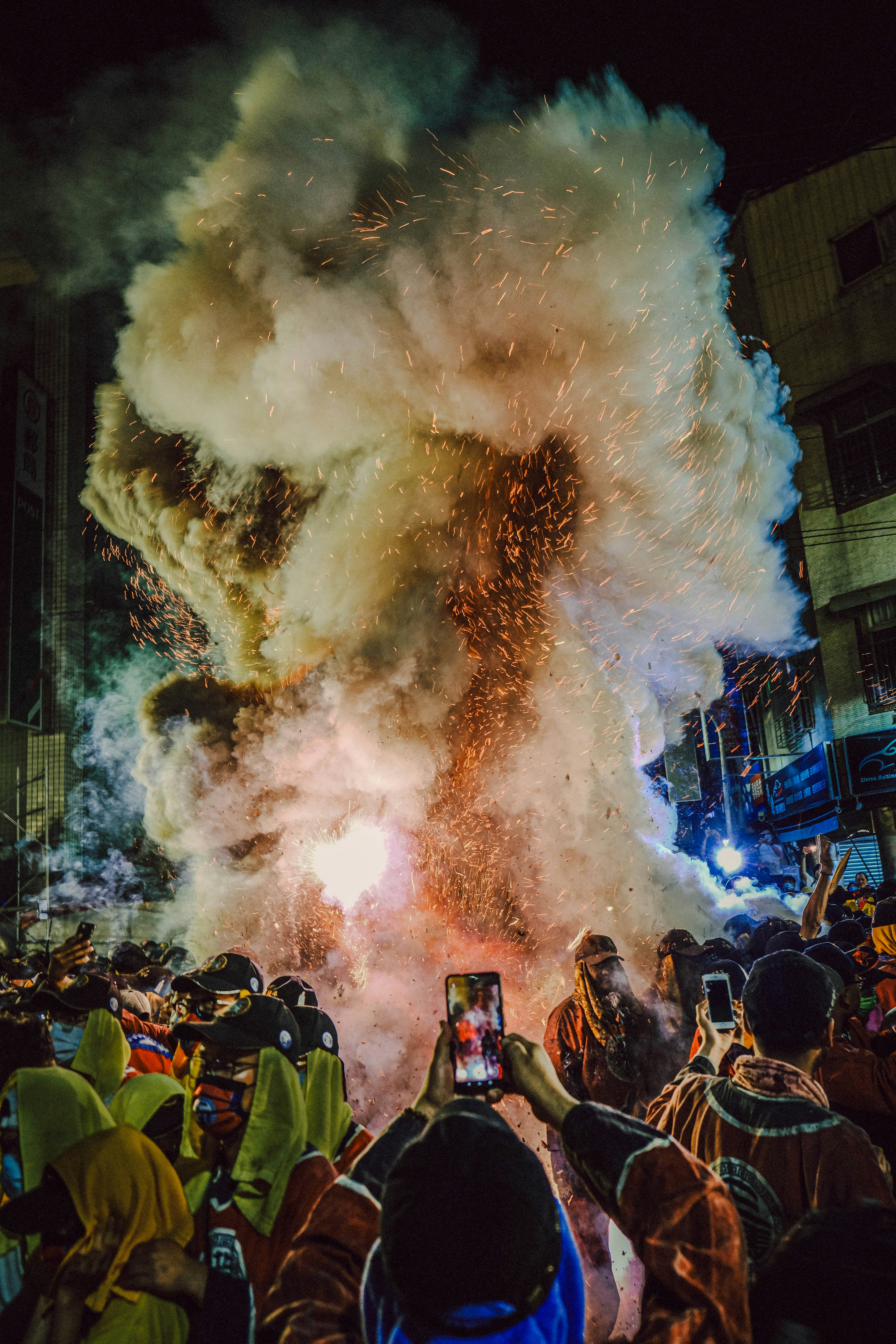 爆煙と火花の中で人々が見守る夜の祭りの群衆