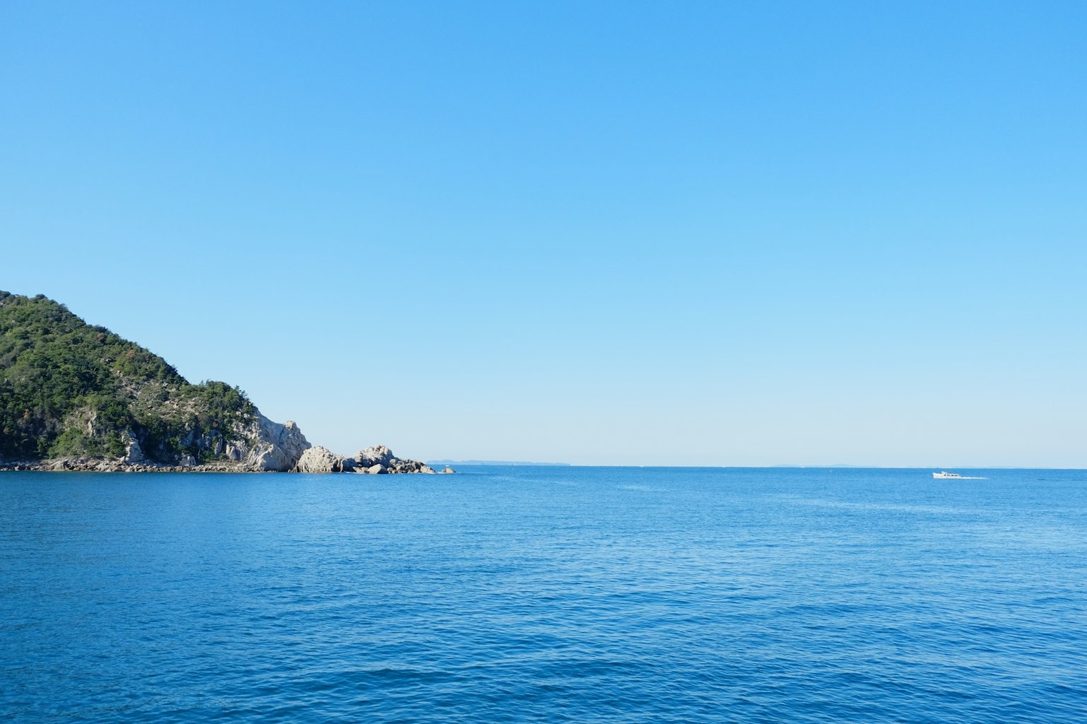 Pemandangan laut biru dan langit cerah dengan bukit hijau di latar belakang