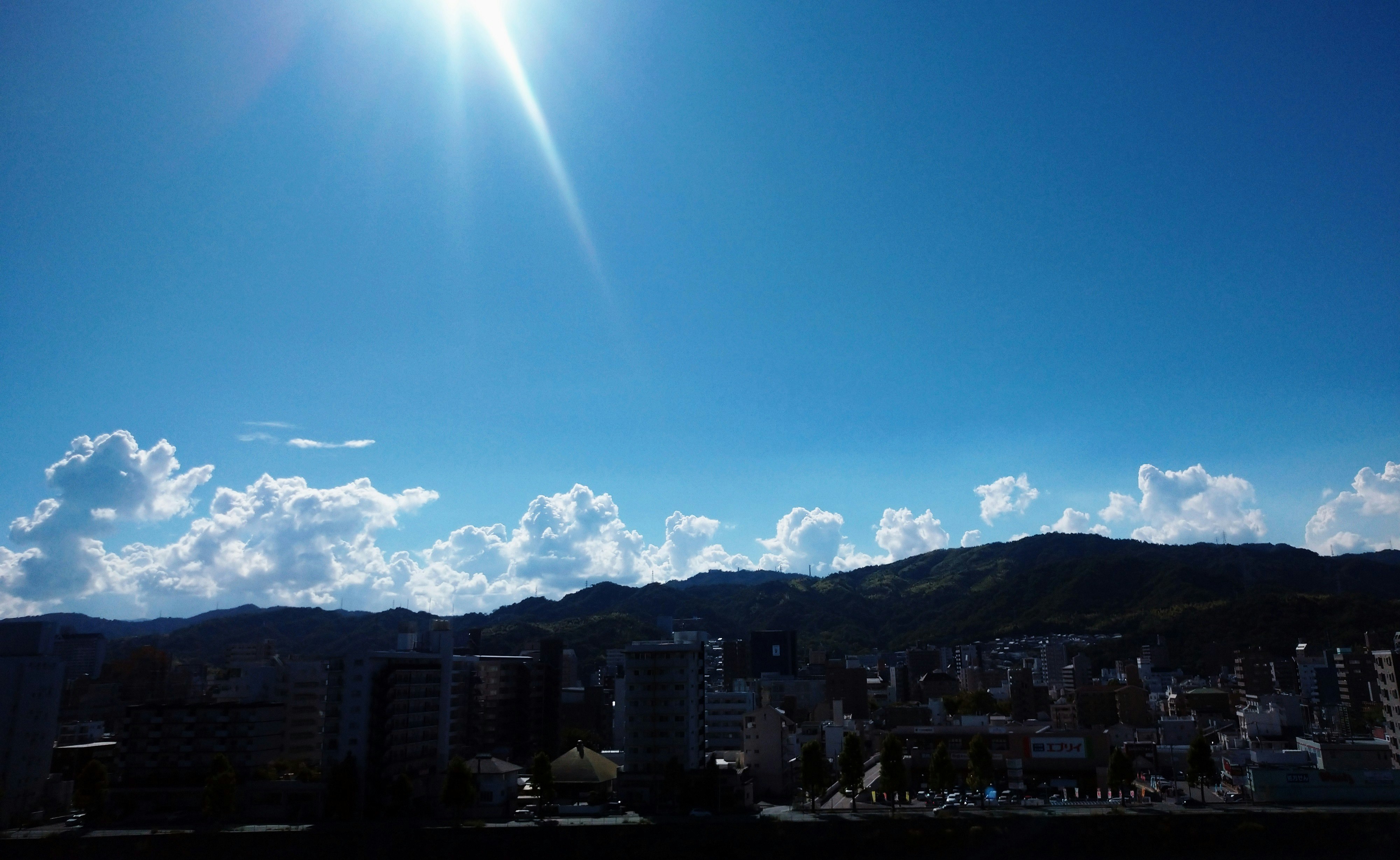 晴れ空の下に広がる雲と山並みの街並み