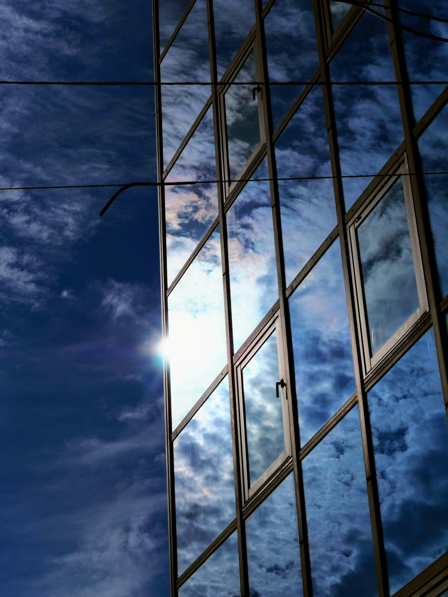 Façade en verre d'un bâtiment reflétant le ciel bleu et les nuages