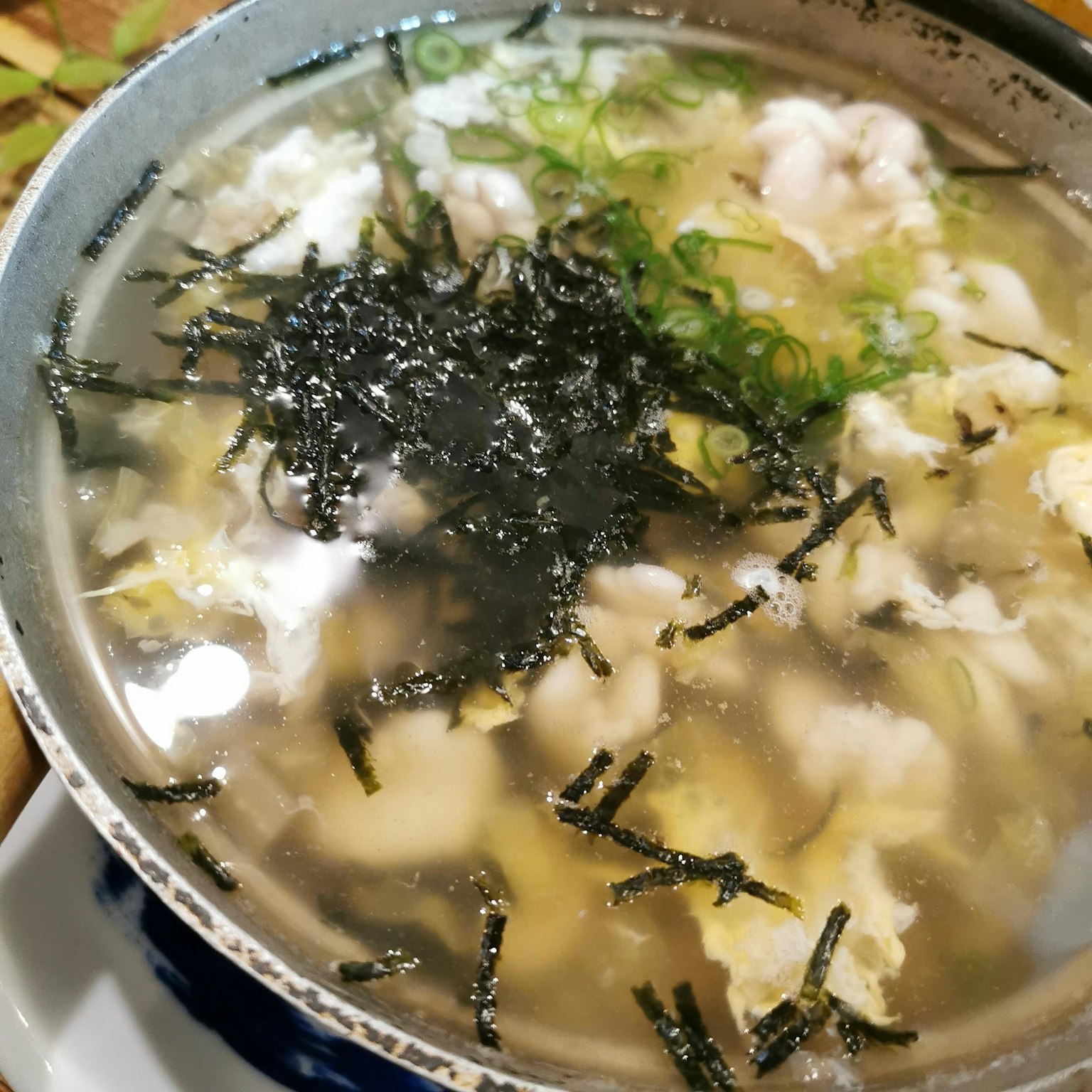 Un tazón de sopa clara con cebollas verdes y algas flotantes