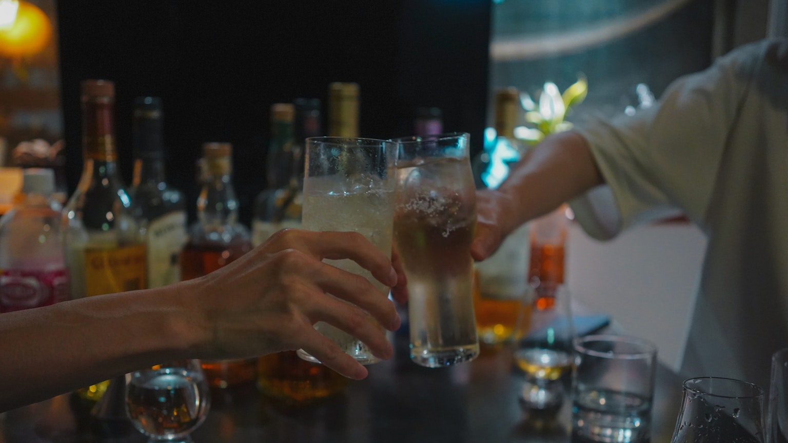 Un momento de brindis con bebidas en mano rodeado de varias botellas de licor