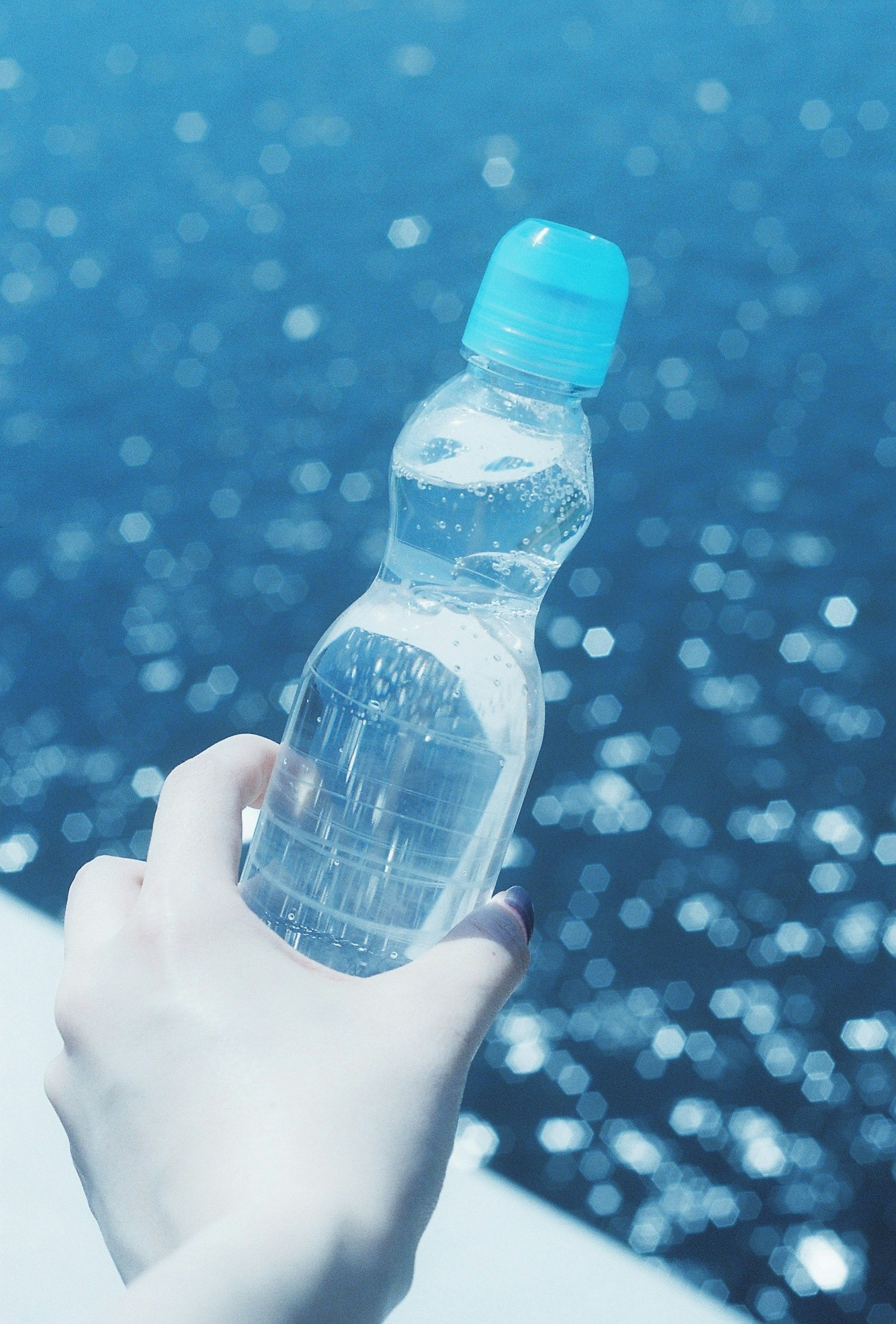 Mano che tiene una bottiglia d'acqua contro uno sfondo blu dell'oceano