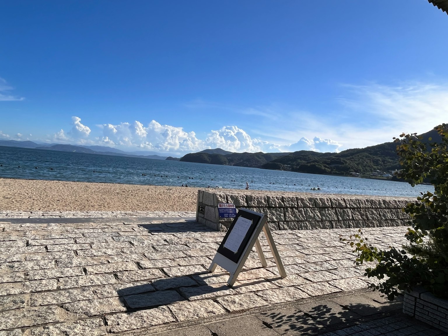 Scena sulla spiaggia con un cartello e un muro di pietra al mare