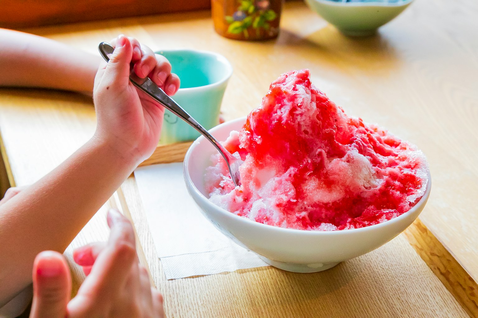 Hand holding a spoon over a bowl of red syrup-covered shaved ice