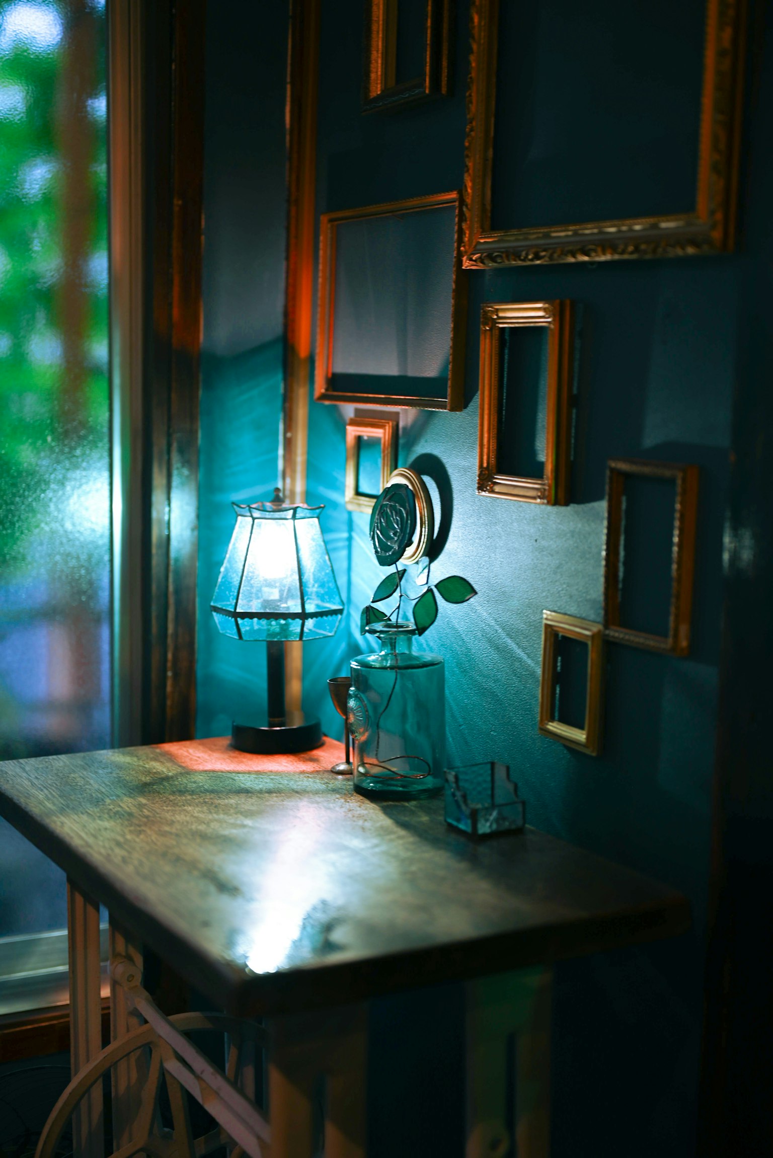 Lámpara de mesa y planta sobre una mesa de madera contra una pared azul con marcos dorados