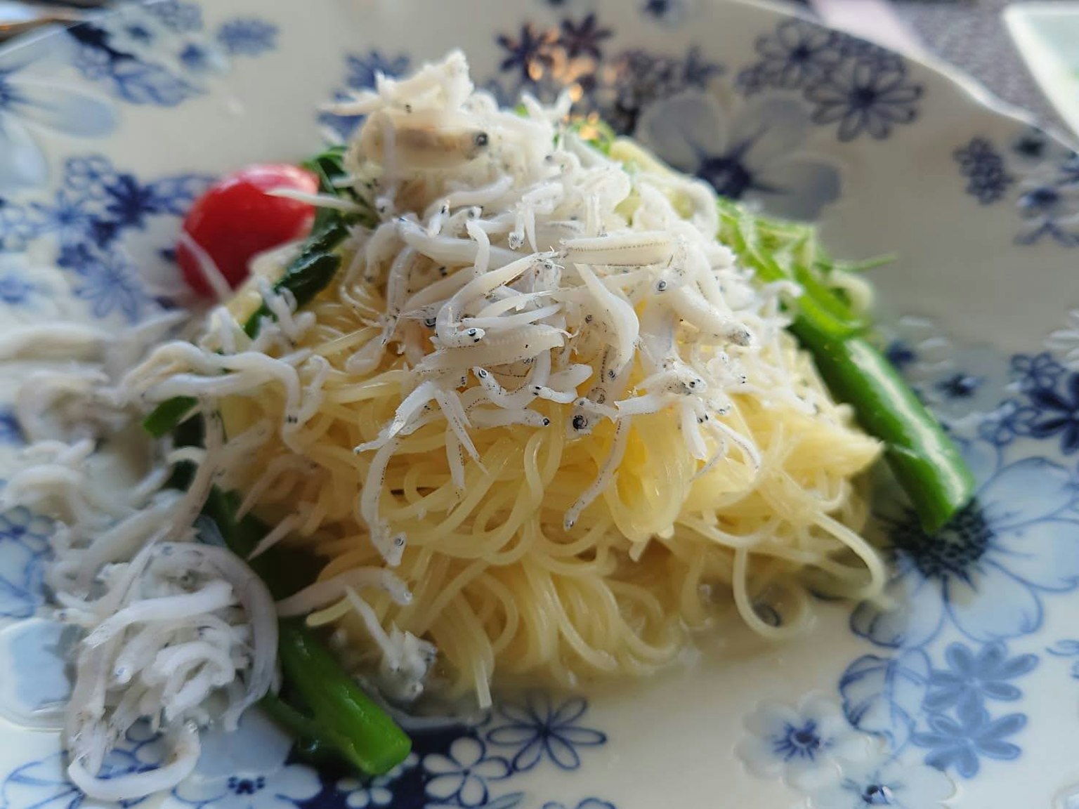 Hidangan pasta halus dengan shirasu dan sayuran di piring berbunga