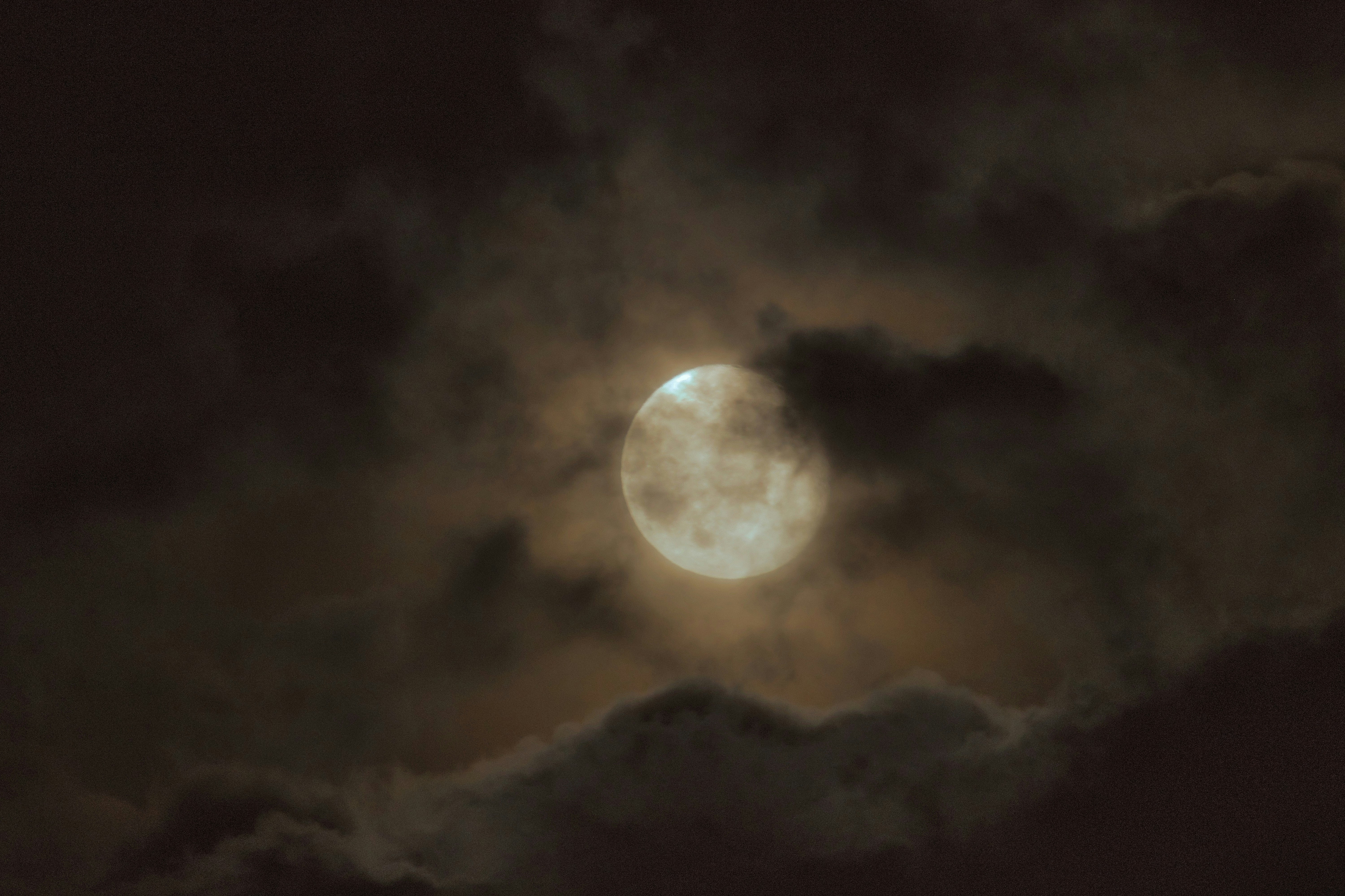 暗い雲に囲まれた明るい満月の夜空
