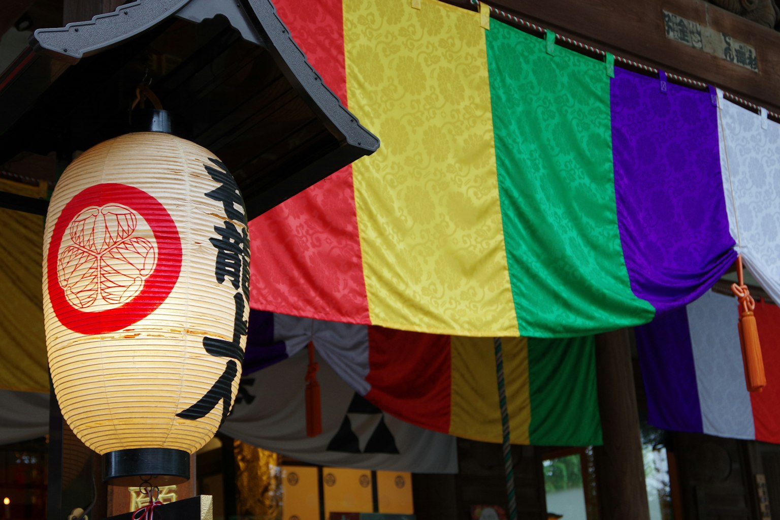 Japanische Laterne mit rotem Kreis und bunten Stoffbahnen in traditioneller Umgebung