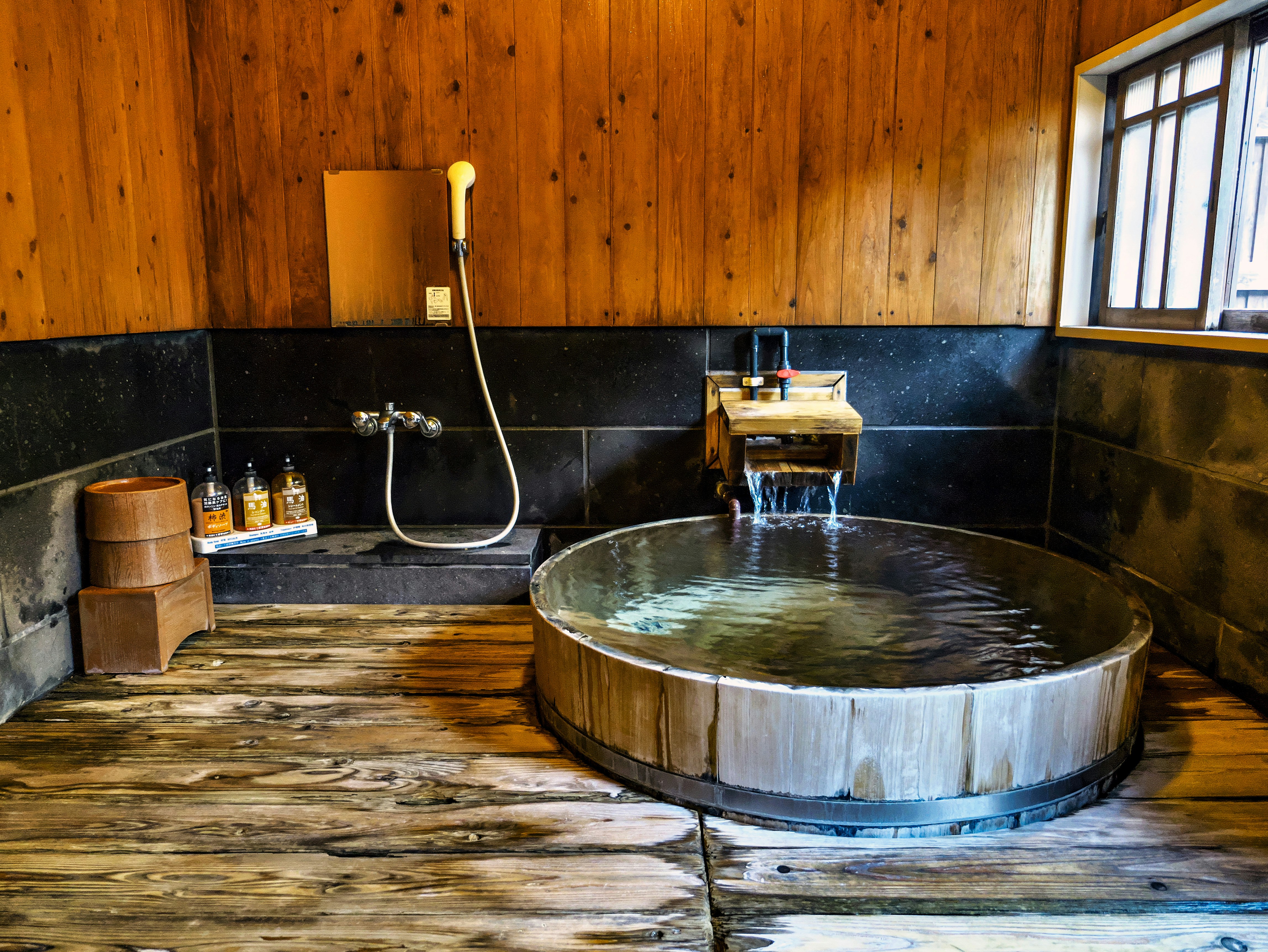 zona de lavado de un baño termal japonés con paredes de madera y tina