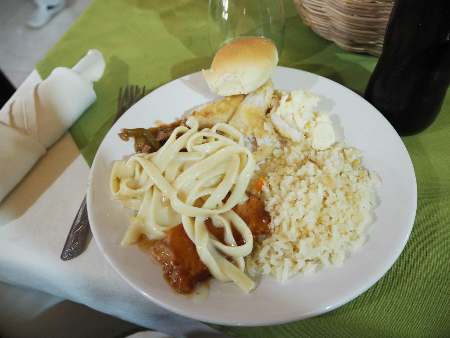 Un plato de comida con pasta, pollo, arroz y un panecillo sobre un mantel verde