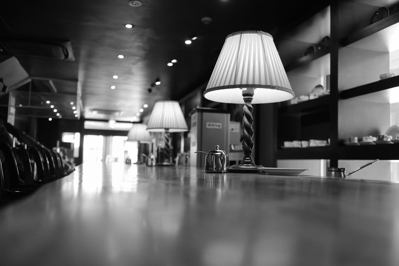 Foto en blanco y negro de un elegante interior de café con lámparas en una mesa y estanterías al fondo