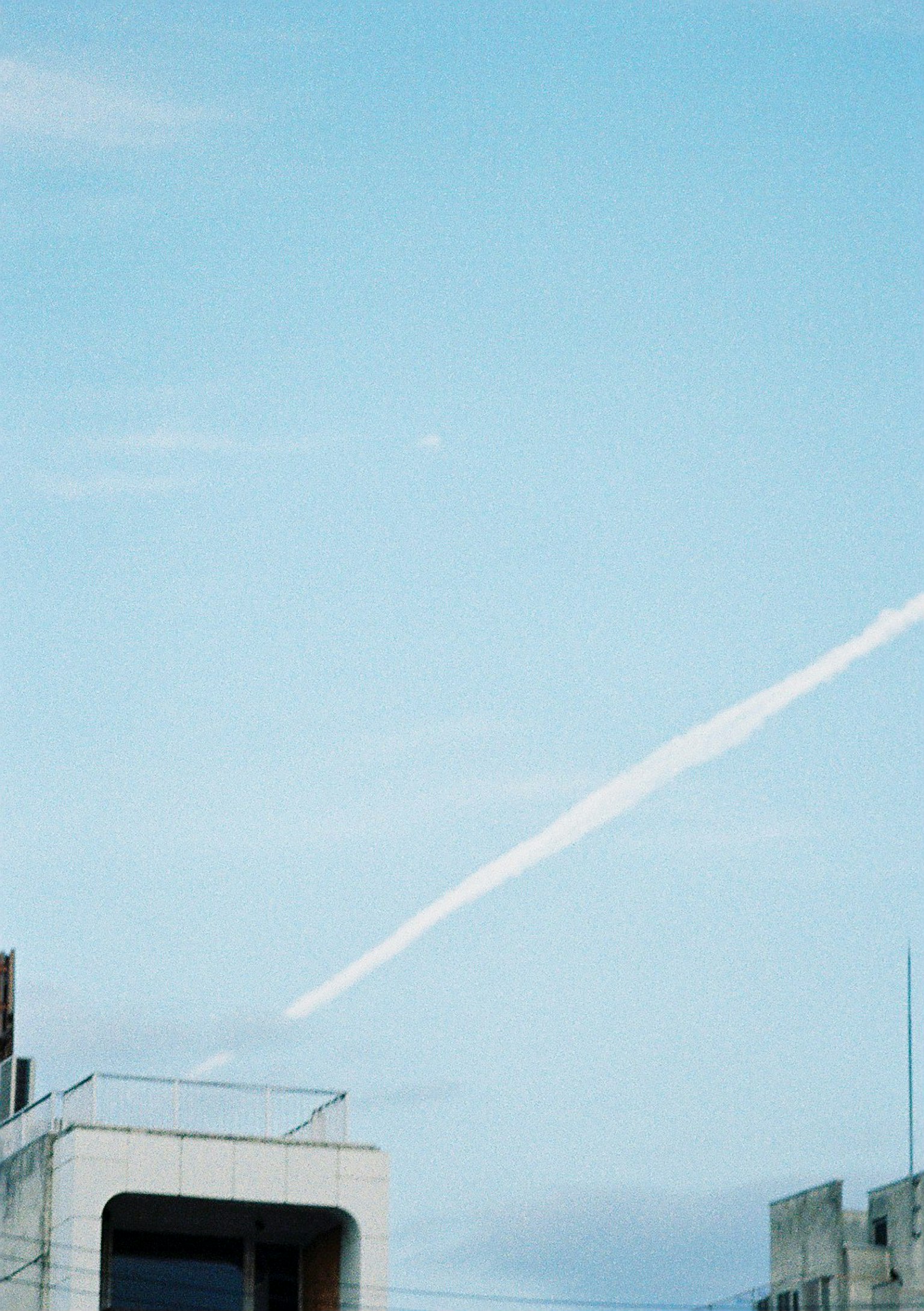 Paisaje urbano con estela de avión en un cielo azul claro