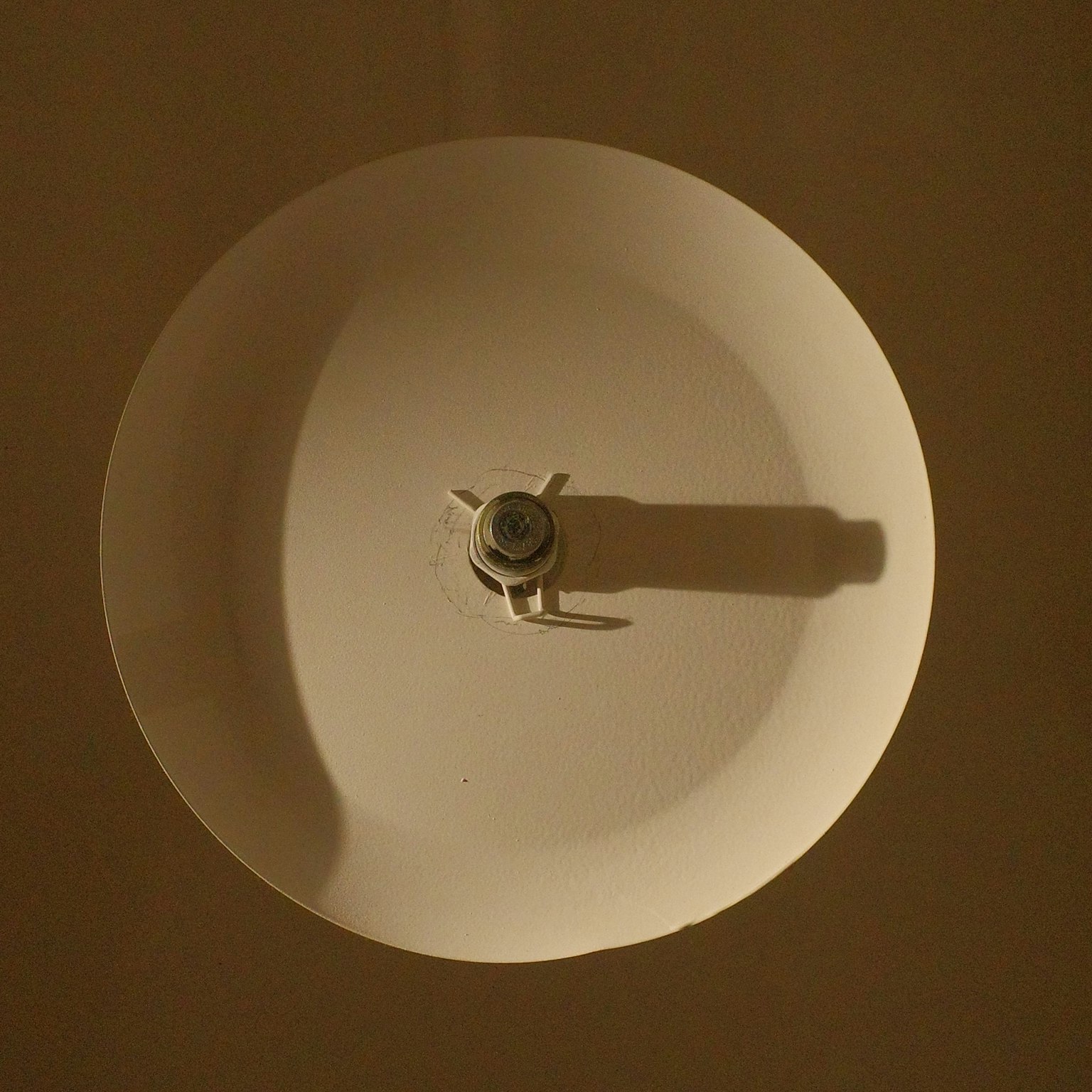 白い円形のランプシェードの上からの視点で中央に金属のソケットが見える