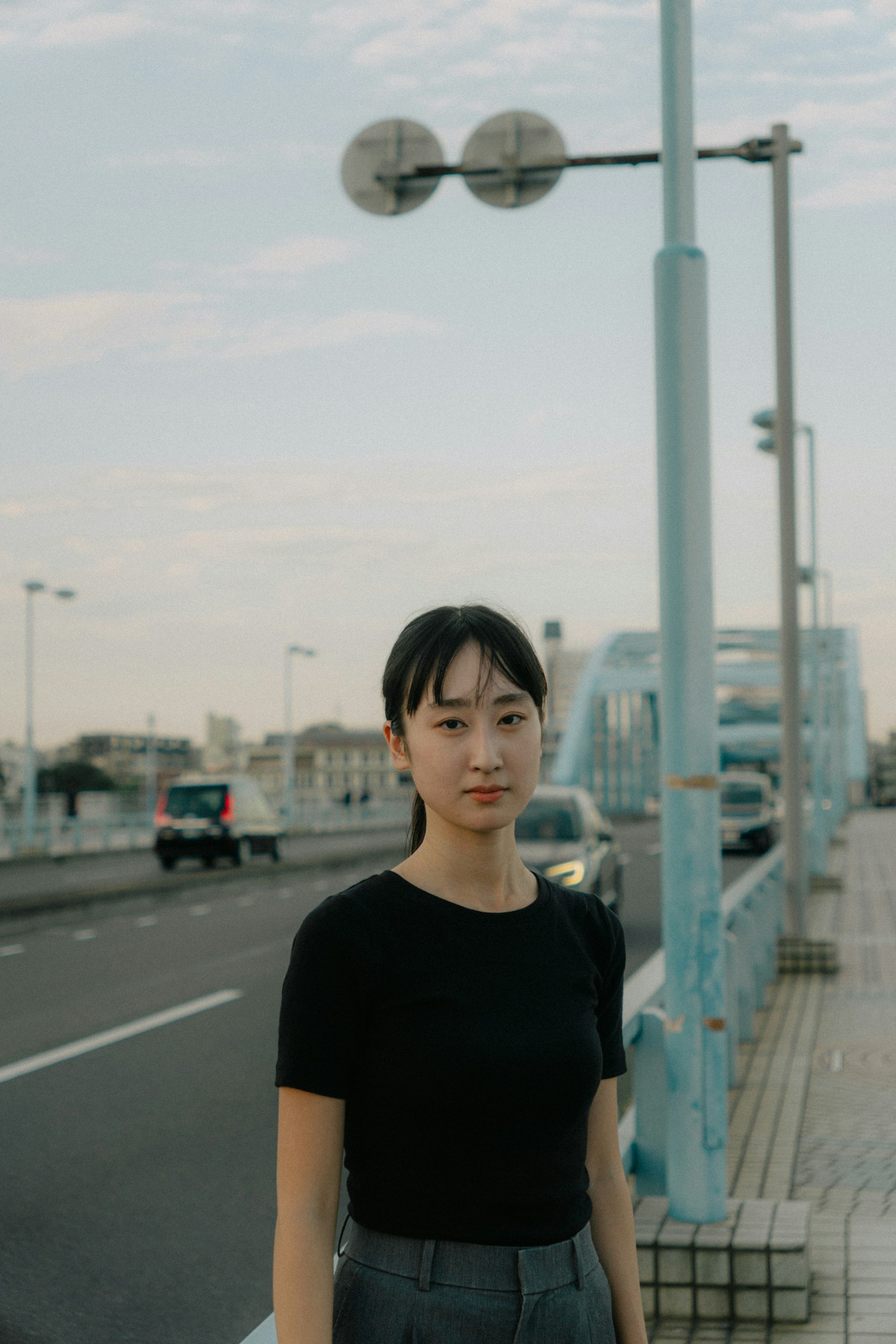 다리 근처에 서 있는 여성의 초상, 검은색 티셔츠를 입고 있음