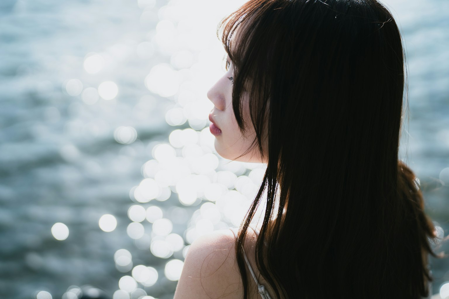 Side profile of a woman looking towards the water with blurred reflections in the background