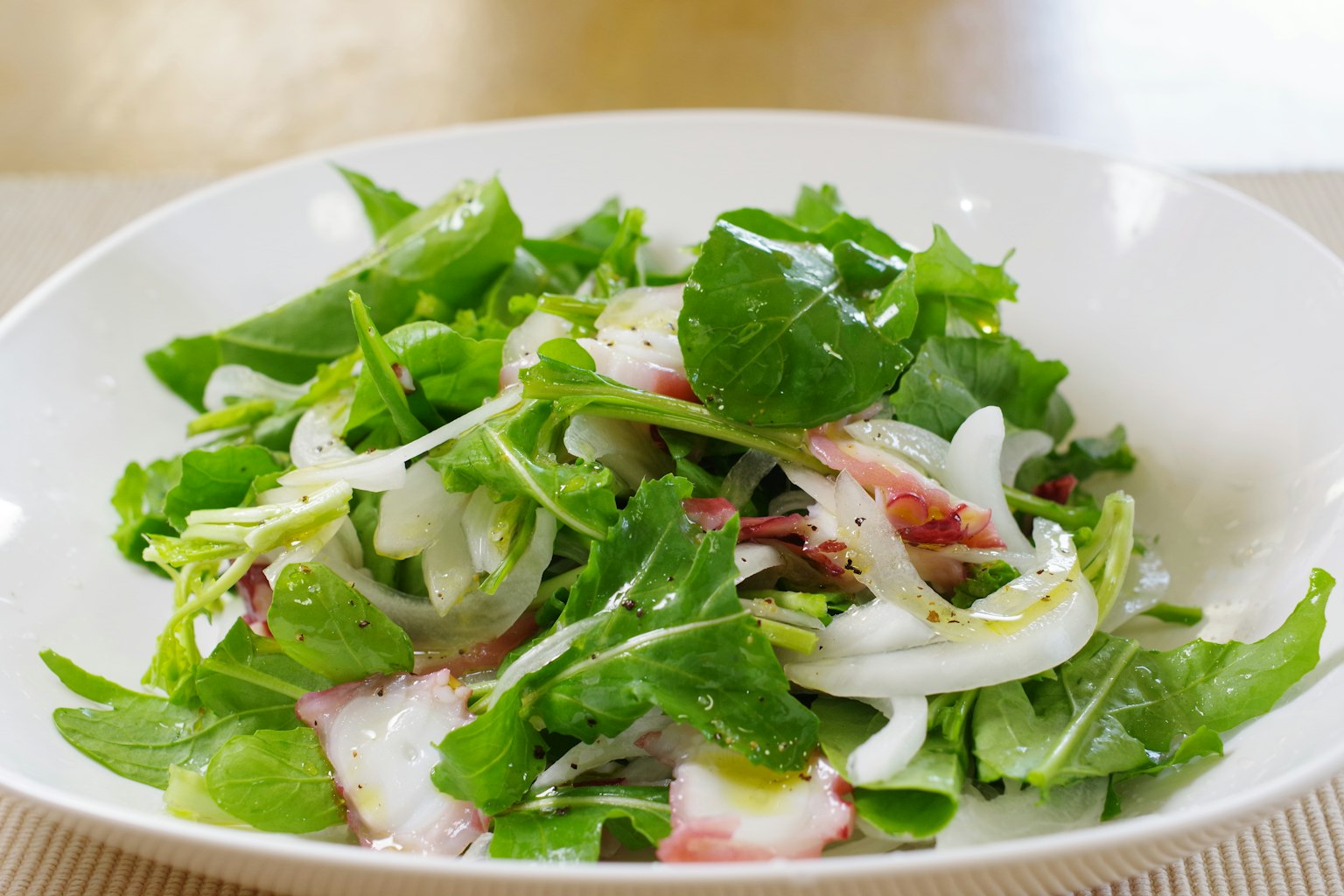 Salade de légumes frais avec des feuilles vertes et des oignons tranchés présentée dans un bol blanc