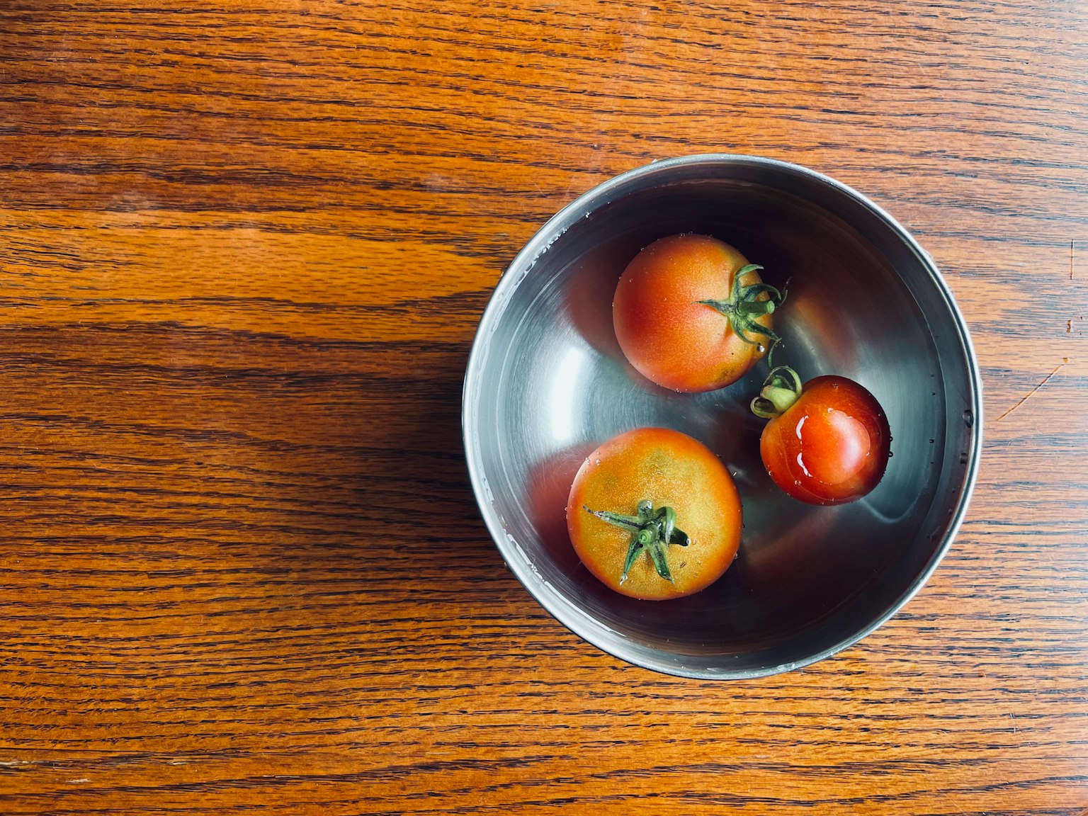 Pomodori rossi che galleggiano in acqua in una ciotola di metallo