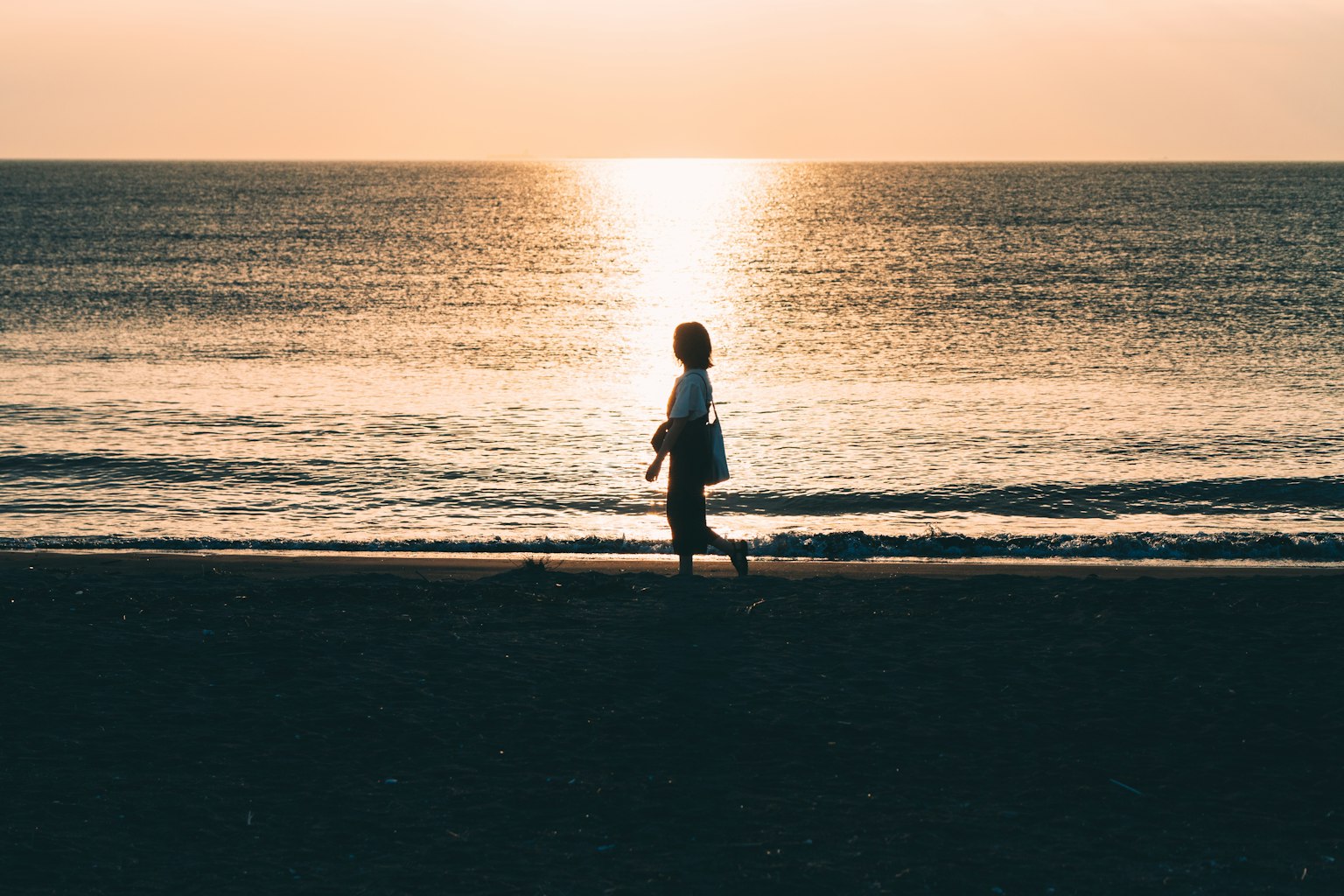 Silhouette of a woman walking along the beach with a sunset in the background