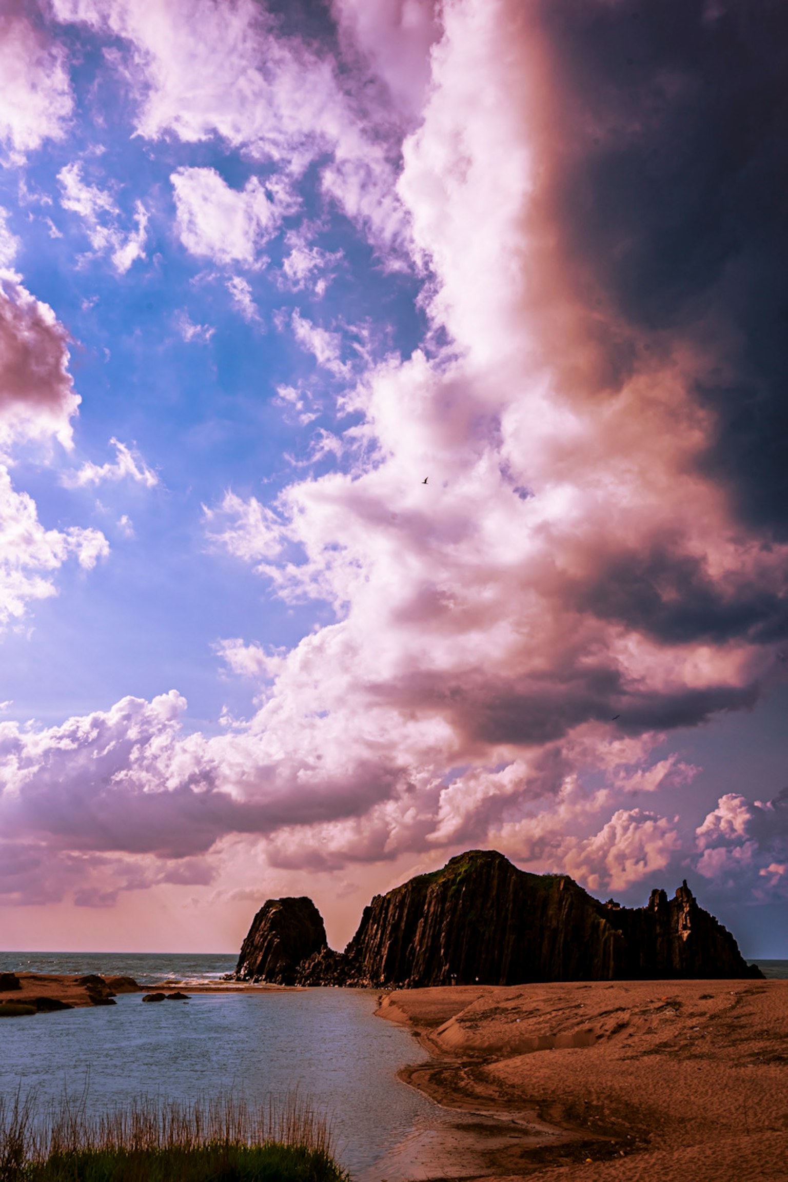 Küstenlandschaft mit einer Felsformation und lebhaften Wolken