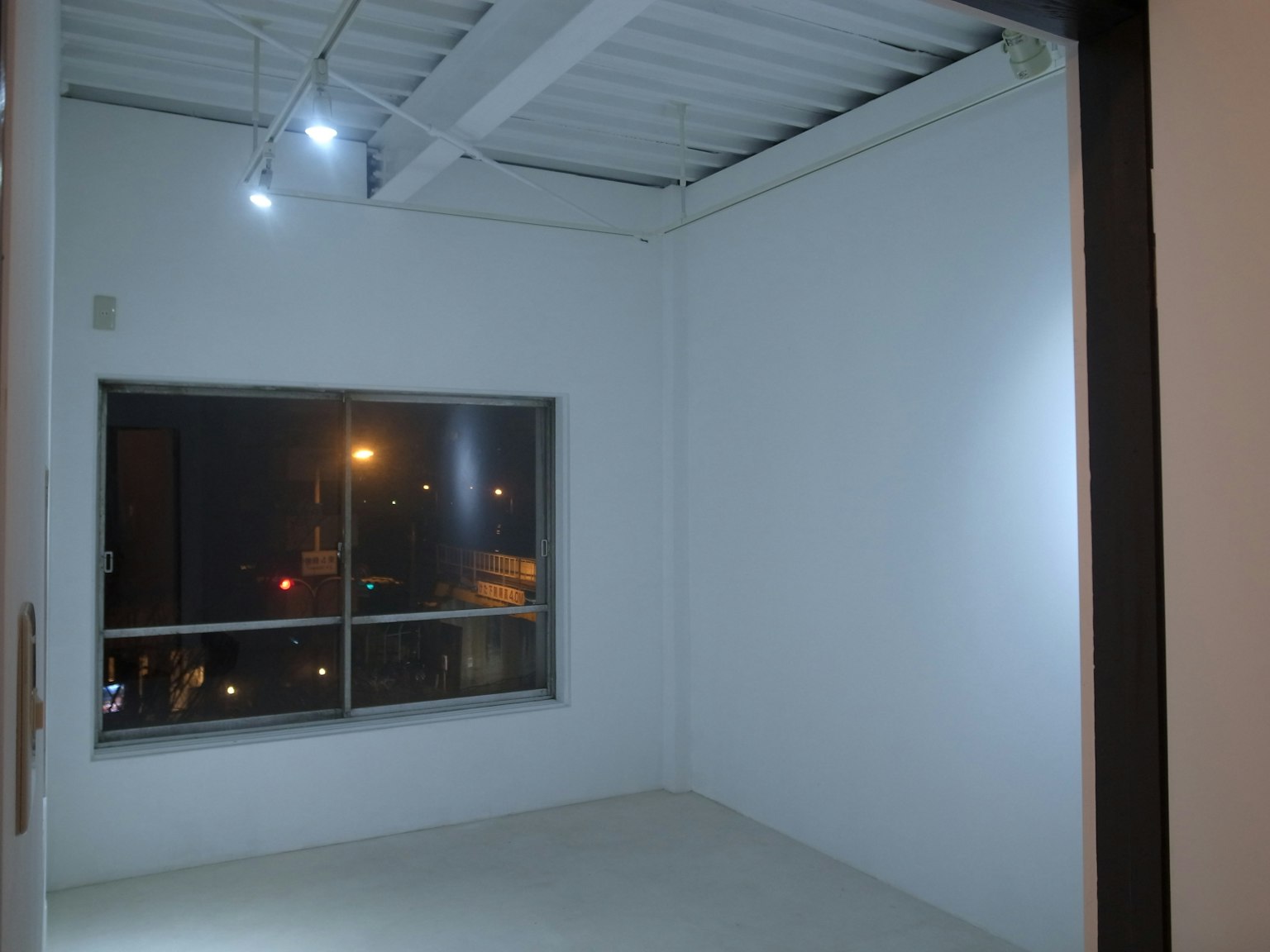 ห้องว่างมีผนังสีขาวและหน้าต่างที่เห็นแสงไฟเมือง