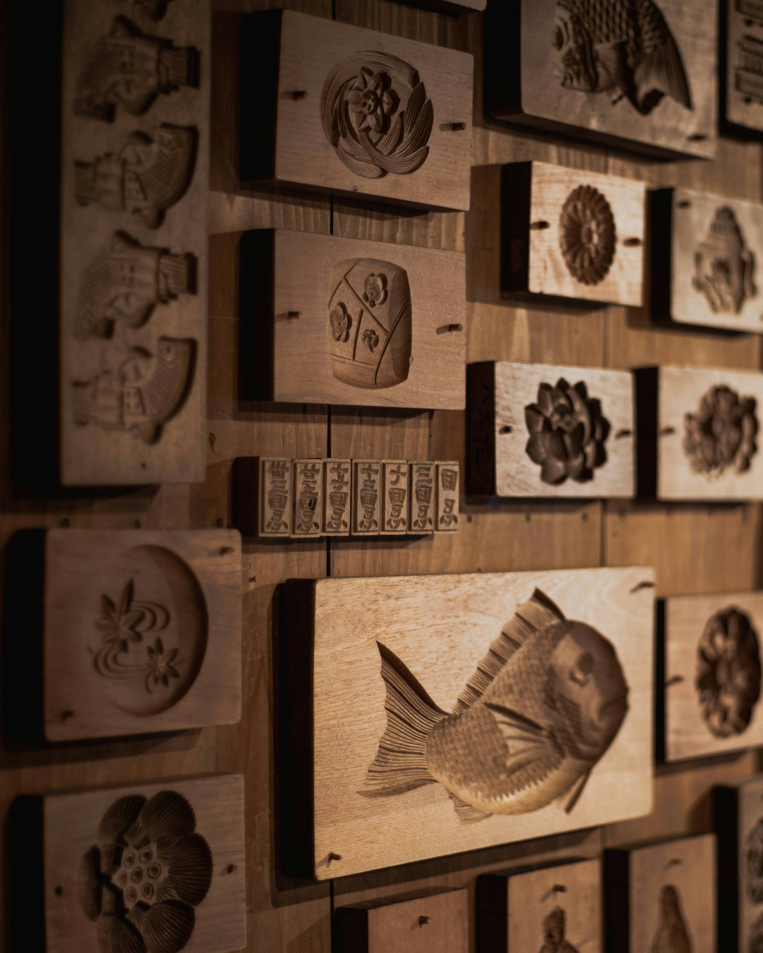 雕刻有鱼和各种图案的木模具展示在墙上
