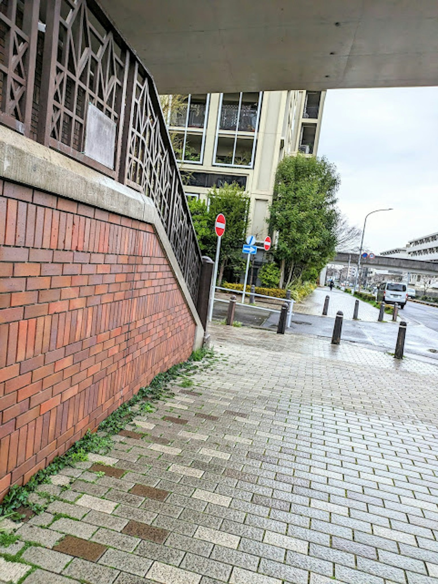 Vista de una pared de ladrillos y una acera pavimentada con un edificio al fondo