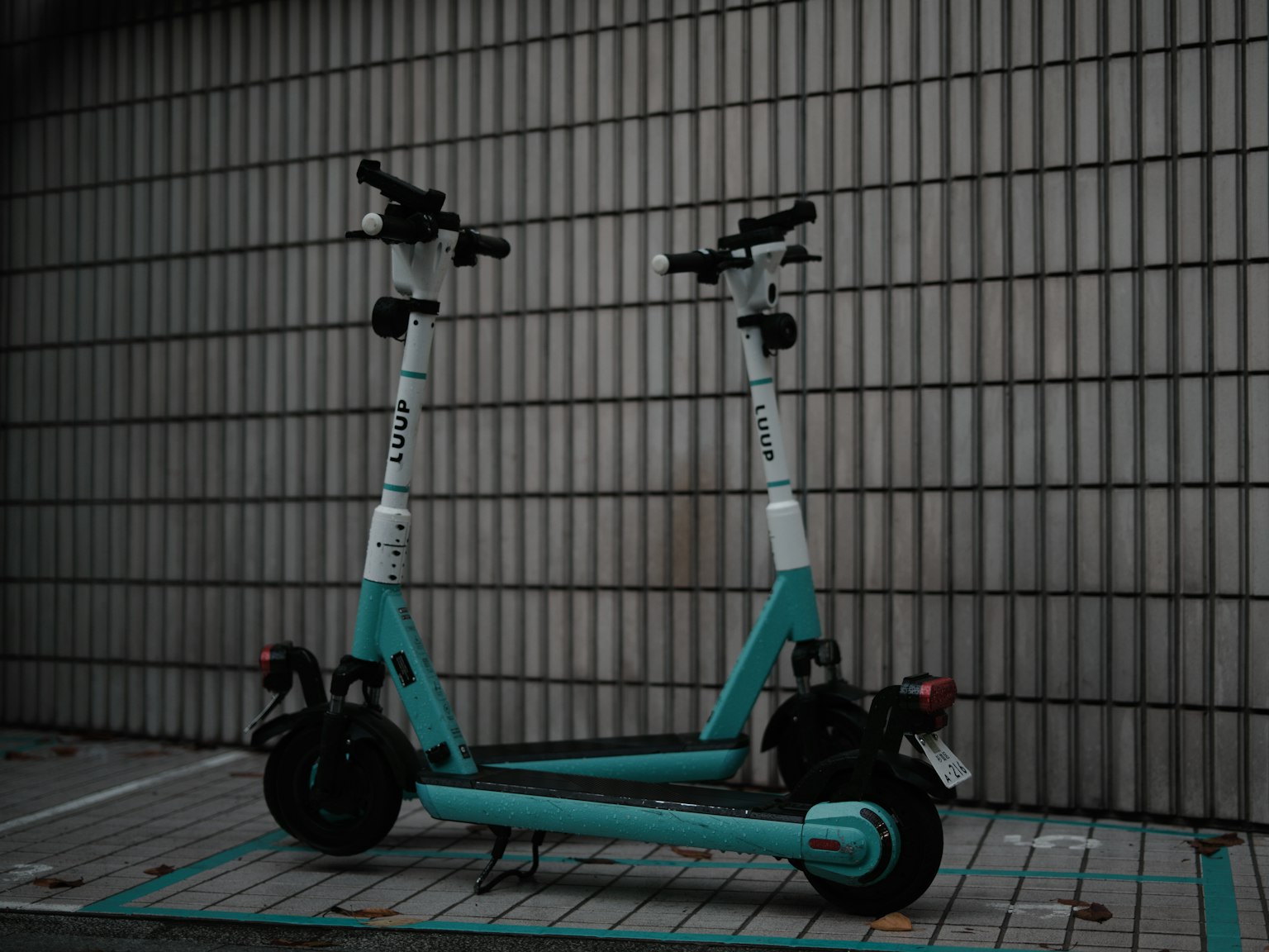 Two turquoise electric scooters parked against a tiled wall