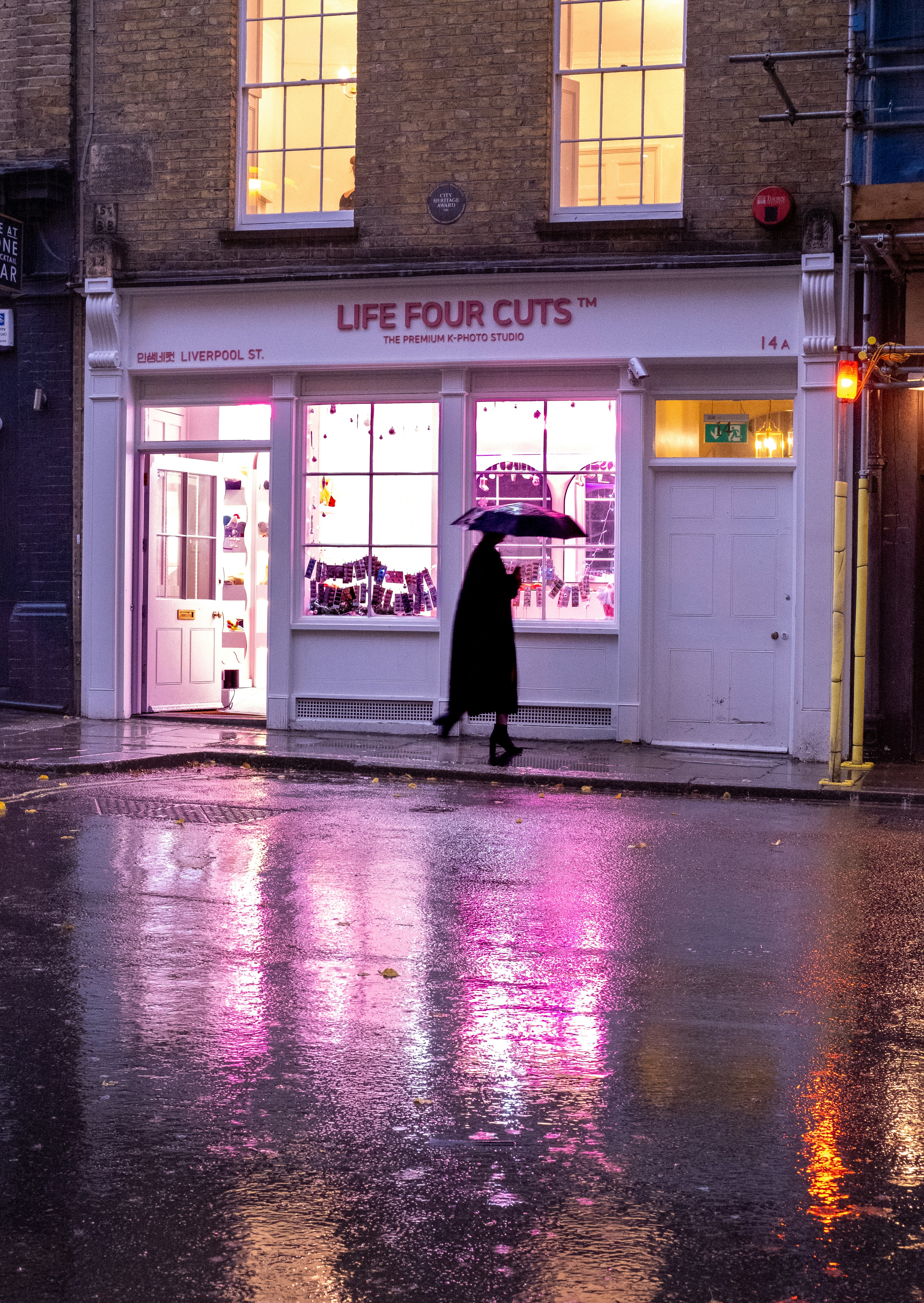 雨の路地に佇む傘をさした人物と店舗のショーウィンドウ