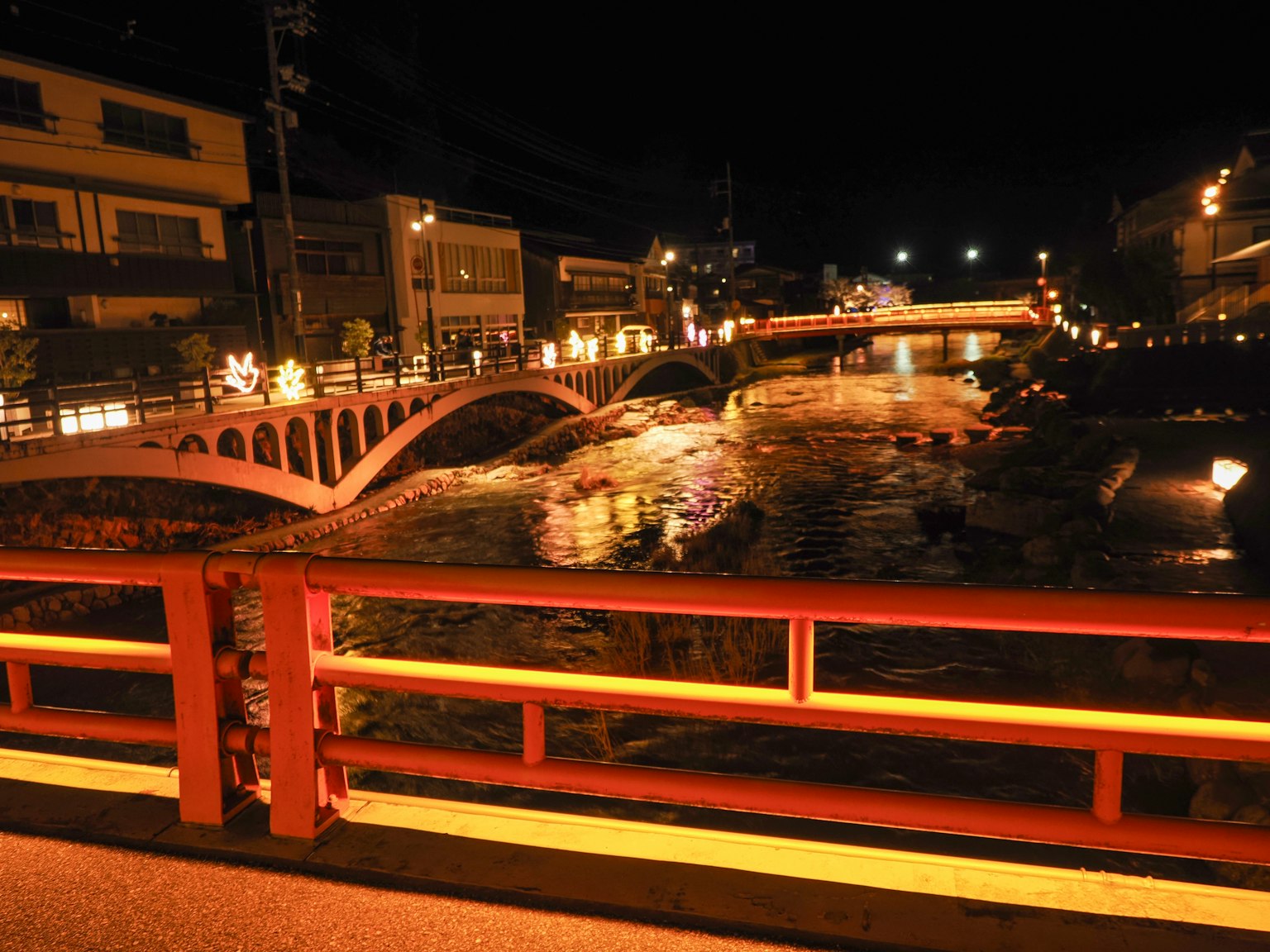 ทิวทัศน์ยามค่ำคืนของเมืองที่มีแม่น้ำและสะพานสีแดง