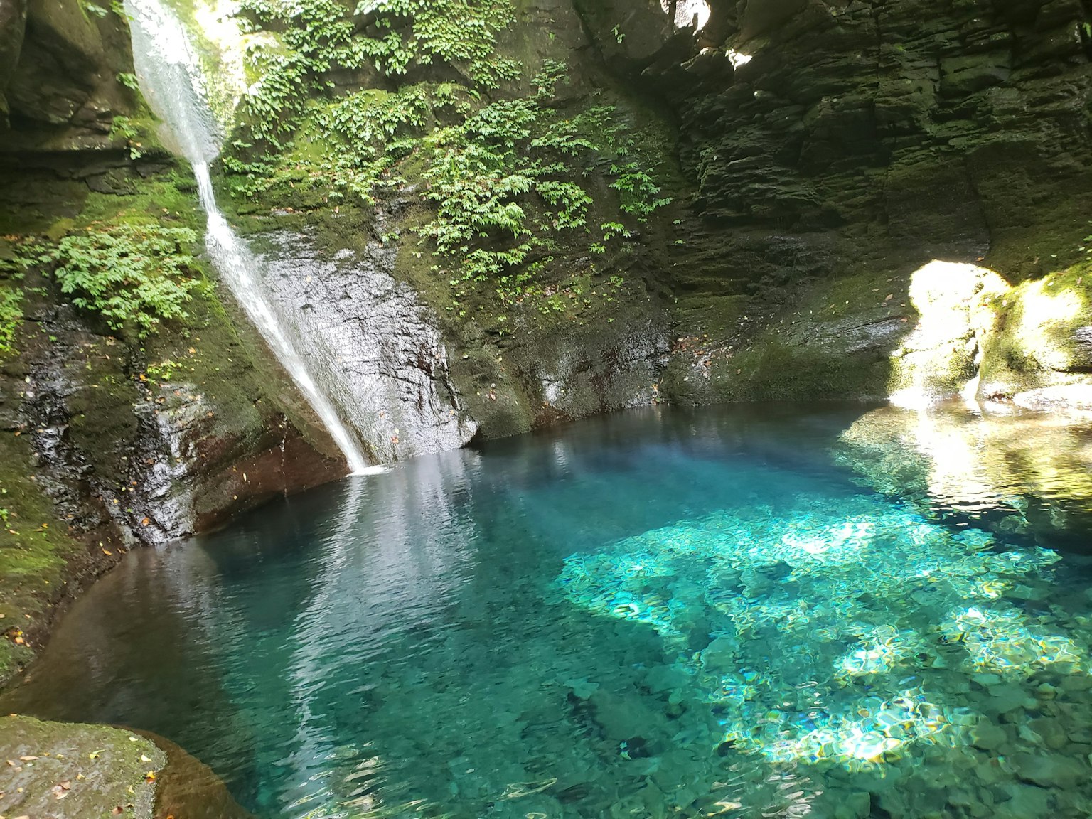 Air terjun yang indah mengalir ke dalam ngarai hijau subur dengan air biru jernih
