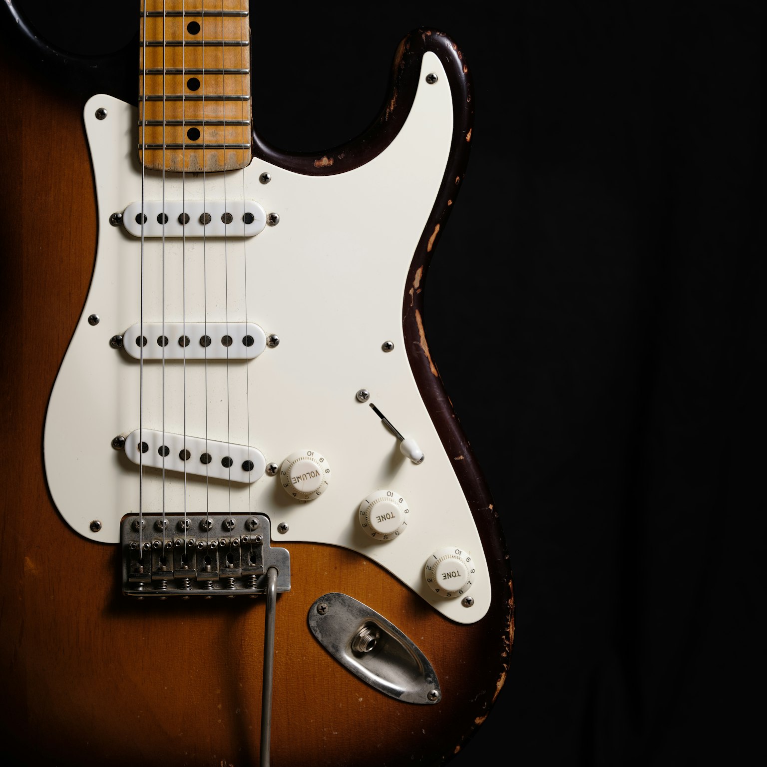Close-up image of an electric guitar featuring a classic Stratocaster design with beautiful color blend against a dark background