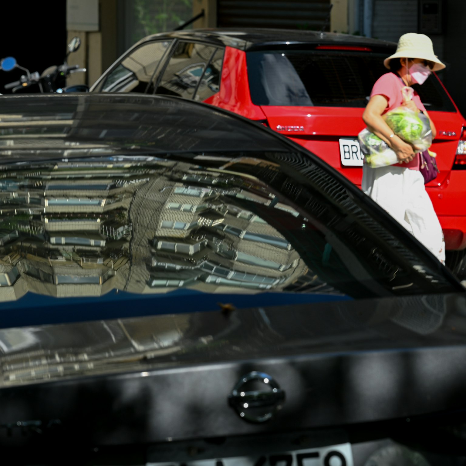 A woman carrying a watermelon walks in front of a black car