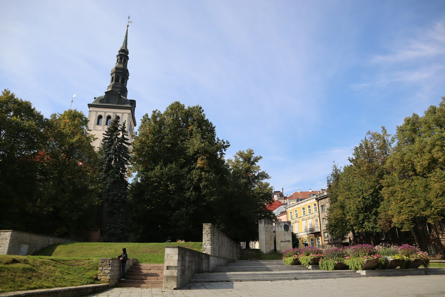 Blick auf einen Park mit einem Turm umgeben von grünen Bäumen und blauem Himmel