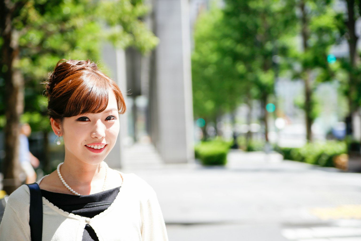 ผู้หญิงยิ้มในสวนด้วยต้นไม้สีเขียวและแสงแดดสว่างเสื้อผ้าลำลองผิวขาว