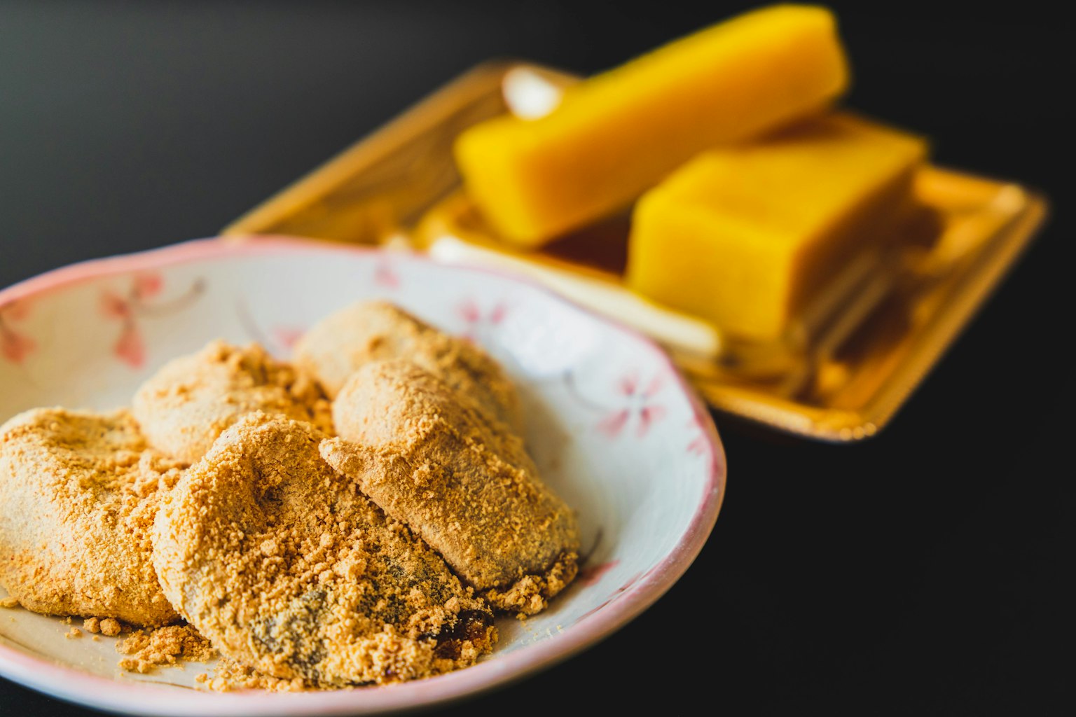一碗裝有黃豆粉團子和背景中黃色日本甜點的圖像