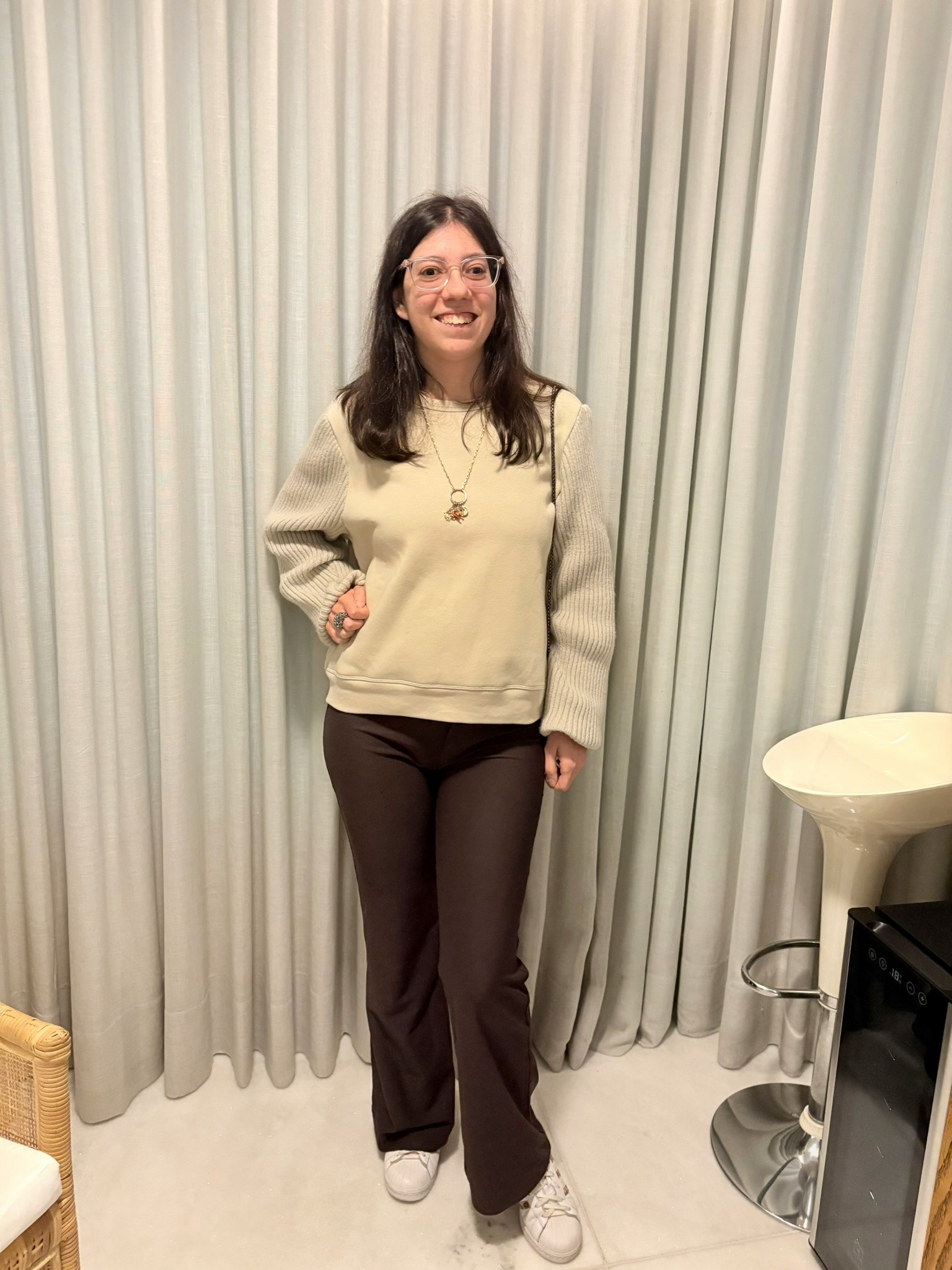 ベージュのニットと白いスニーカーの女性が室内でポーズ