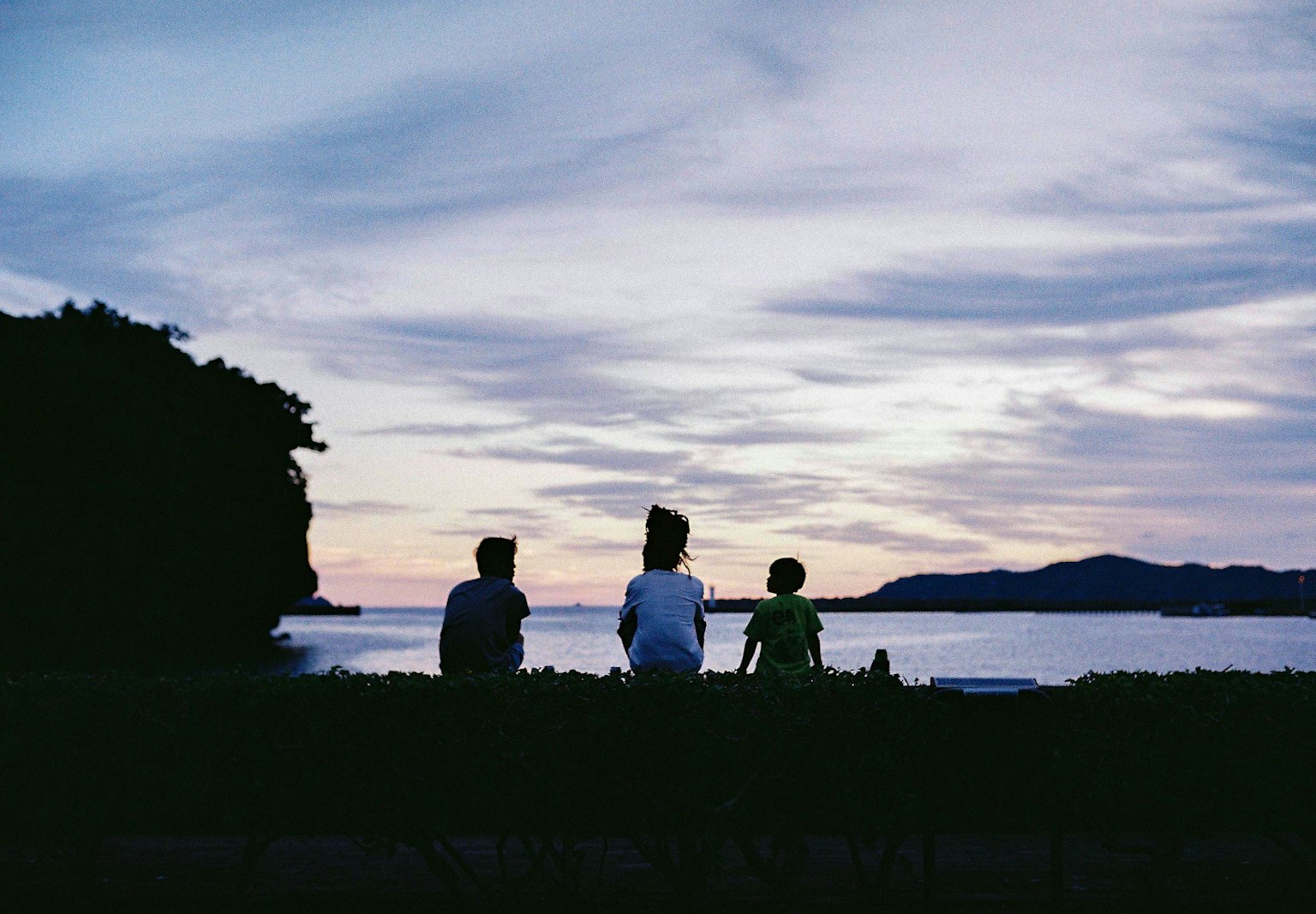 Silhouette di tre persone che guardano il tramonto sul mare