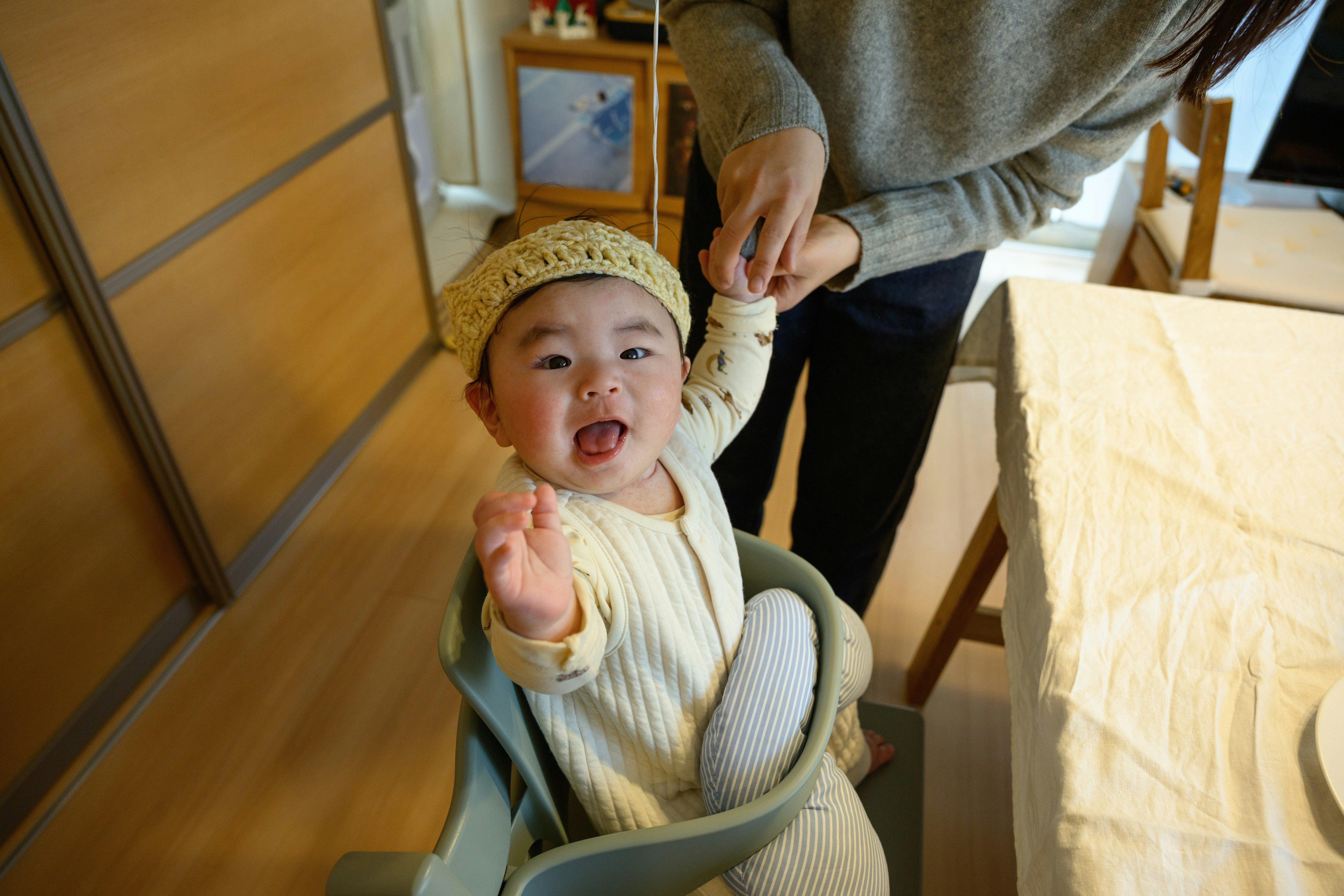 ベビーチェアに座る赤ちゃんと寄り添う大人の手