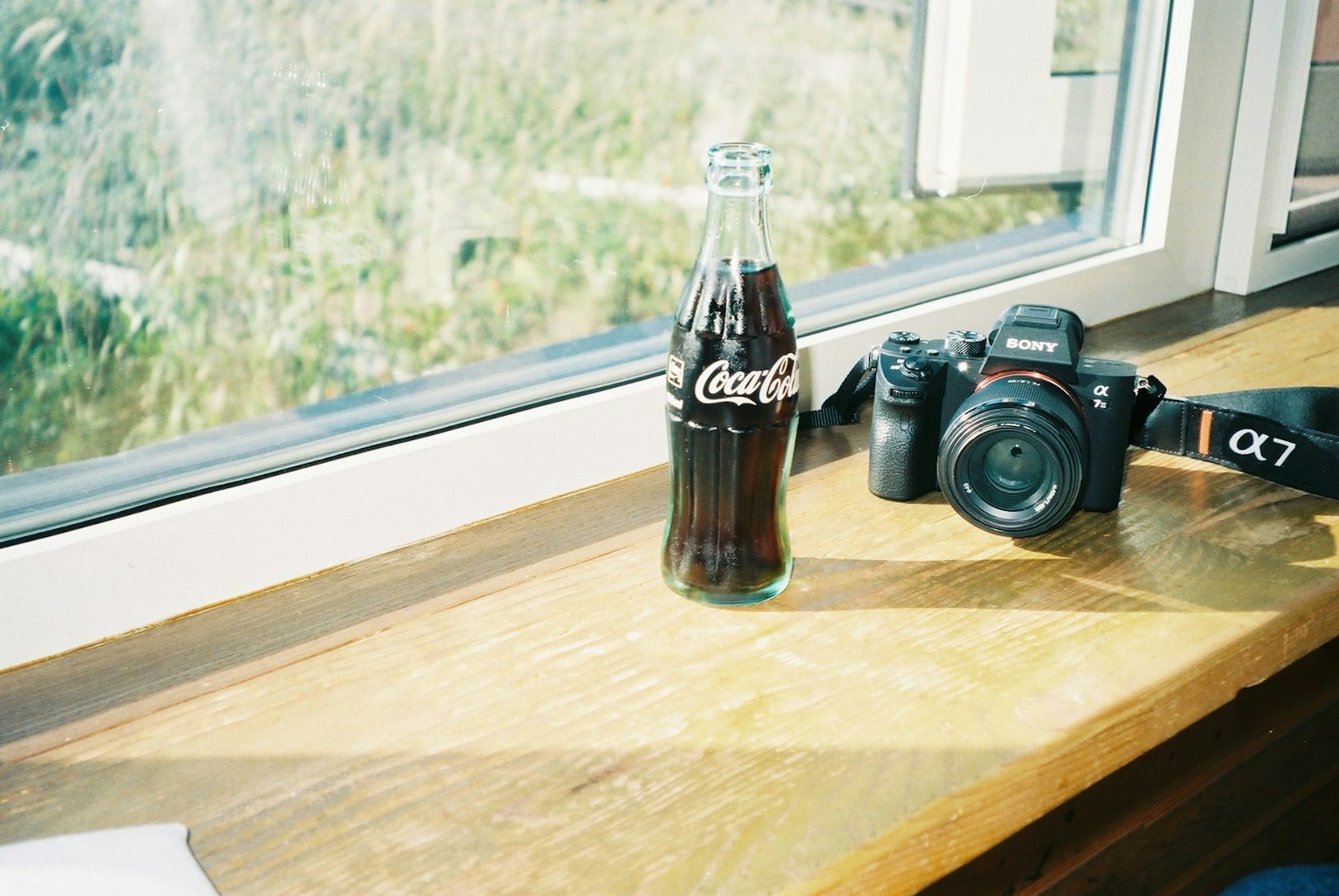 Coca-Cola-Flasche und Kamera auf einem Holztisch am Fenster
