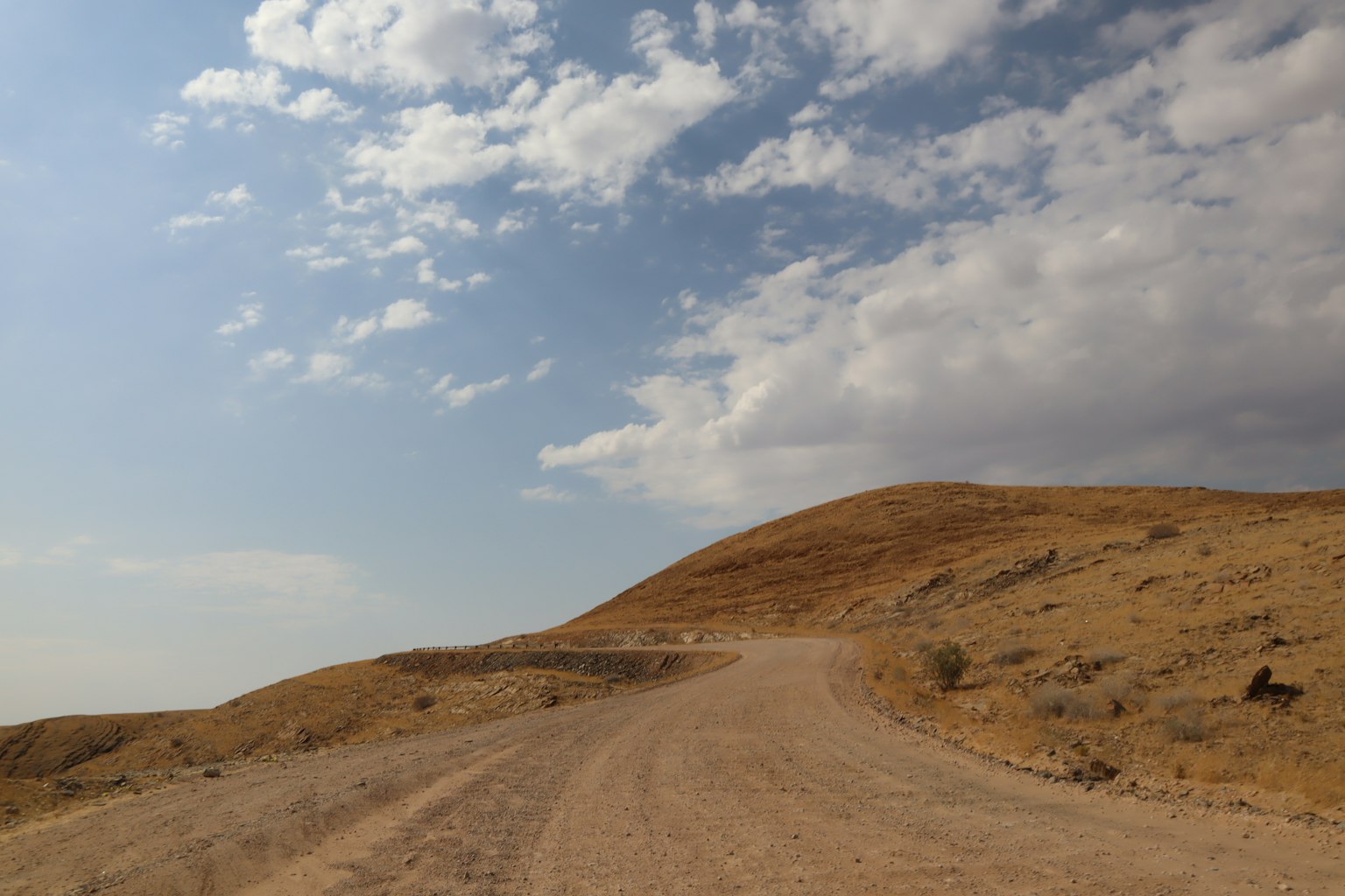 Camino de grava serpenteando a través de colinas áridas bajo un cielo azul