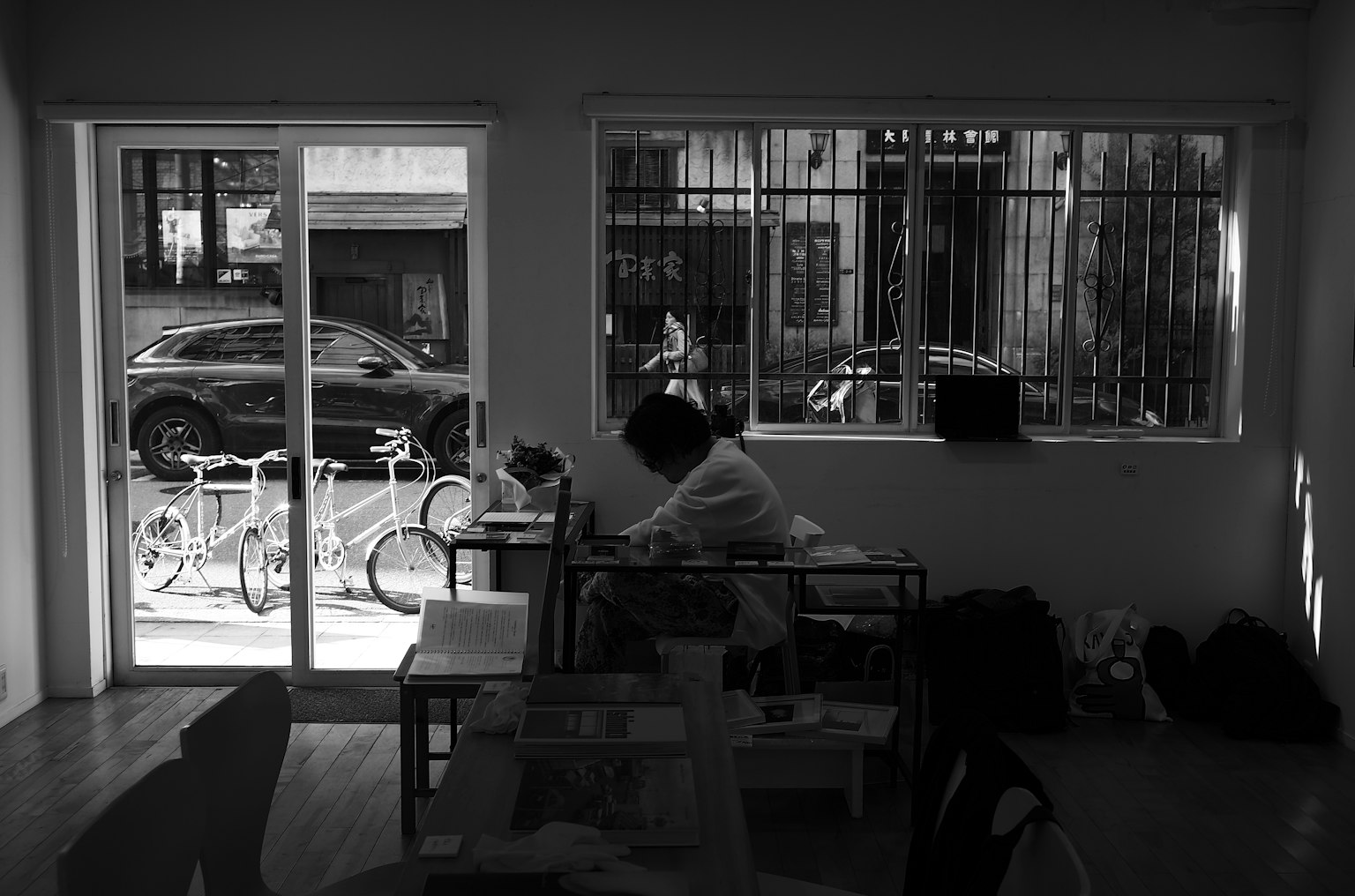 A person working indoors in black and white with bicycles visible outside