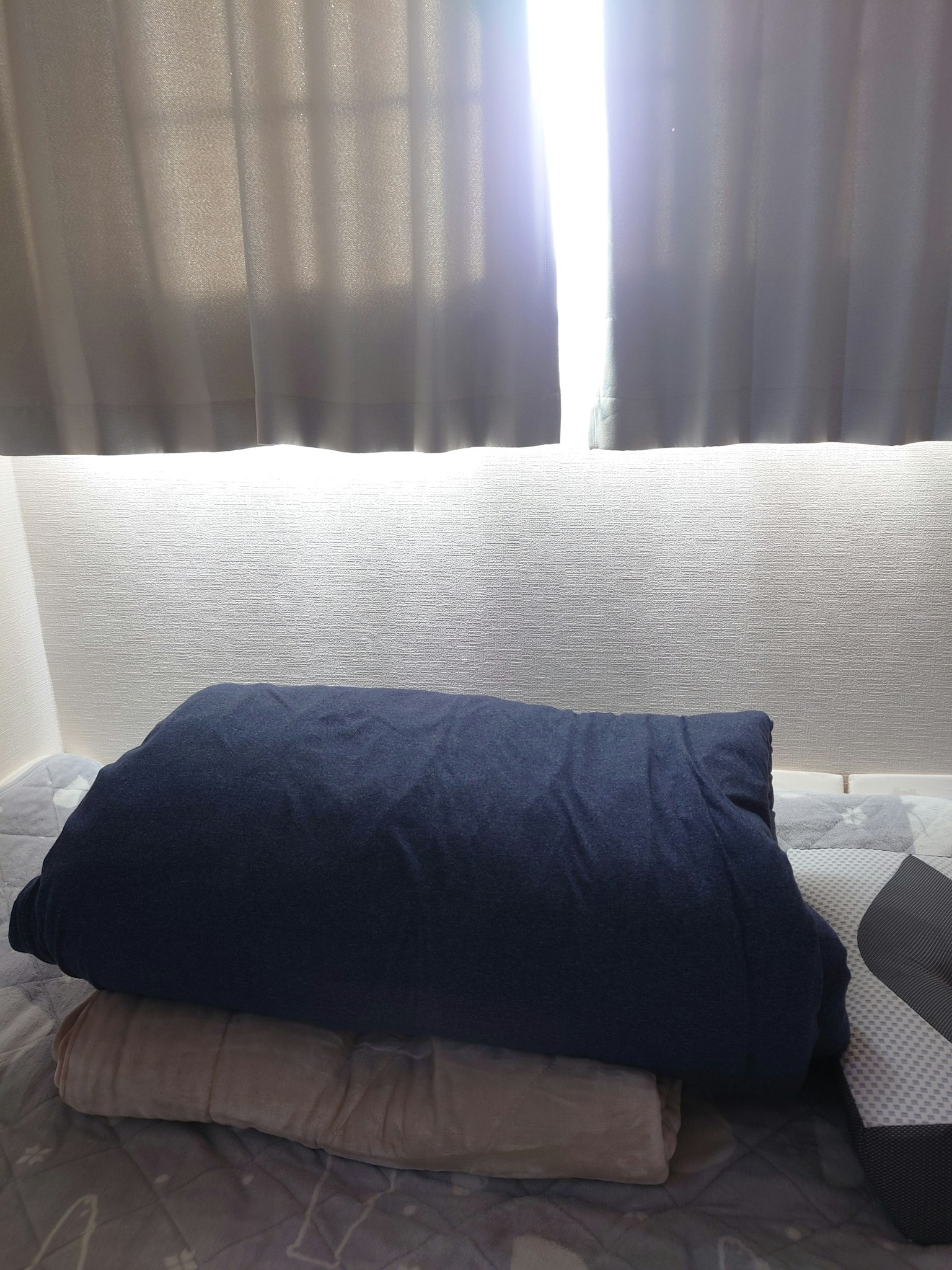 Immagine che mostra una pila di biancheria da letto con una coperta blu navy e un cuscino grigio vicino a una finestra