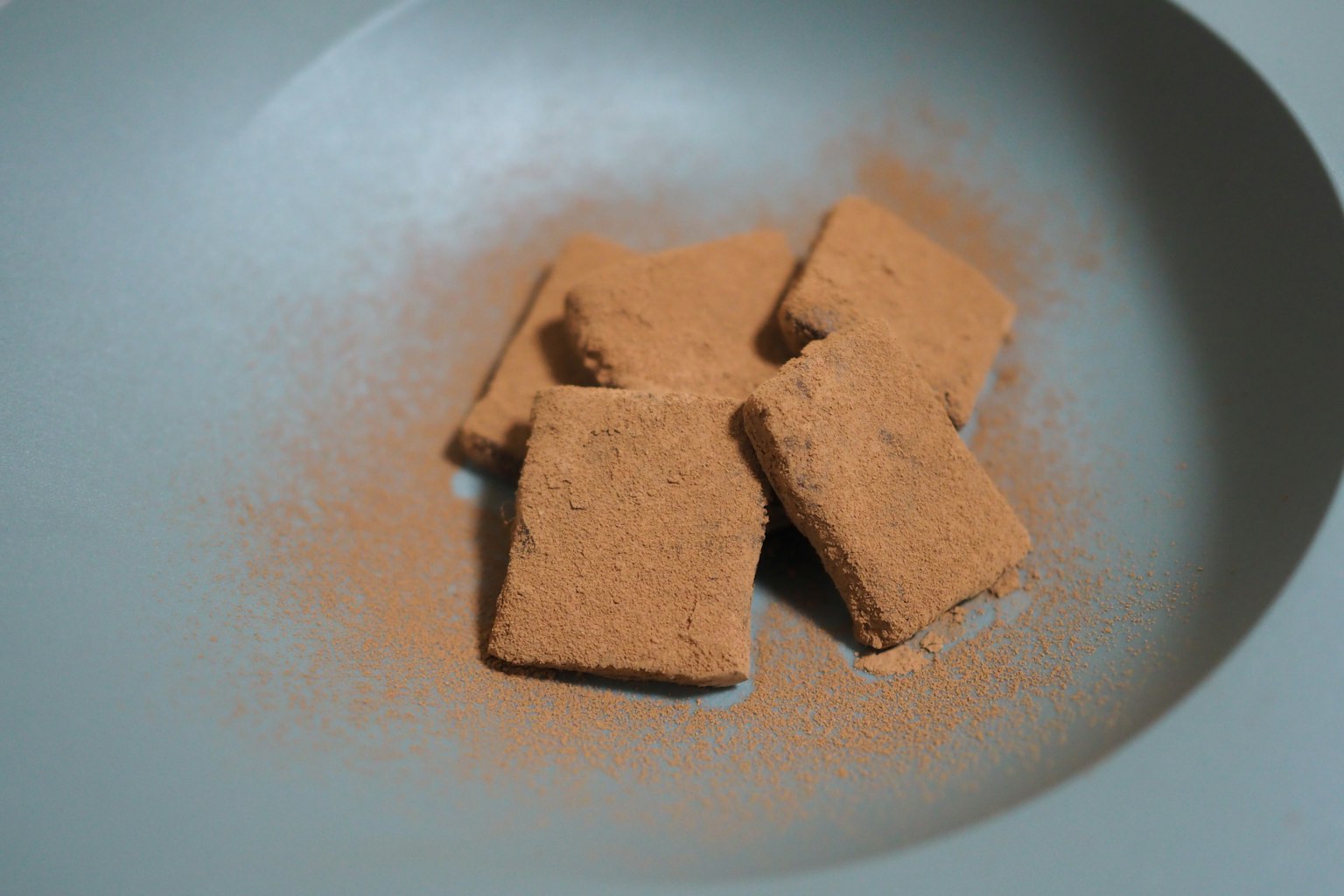Galletas cuadradas en un plato azul con polvo marrón esparcido alrededor
