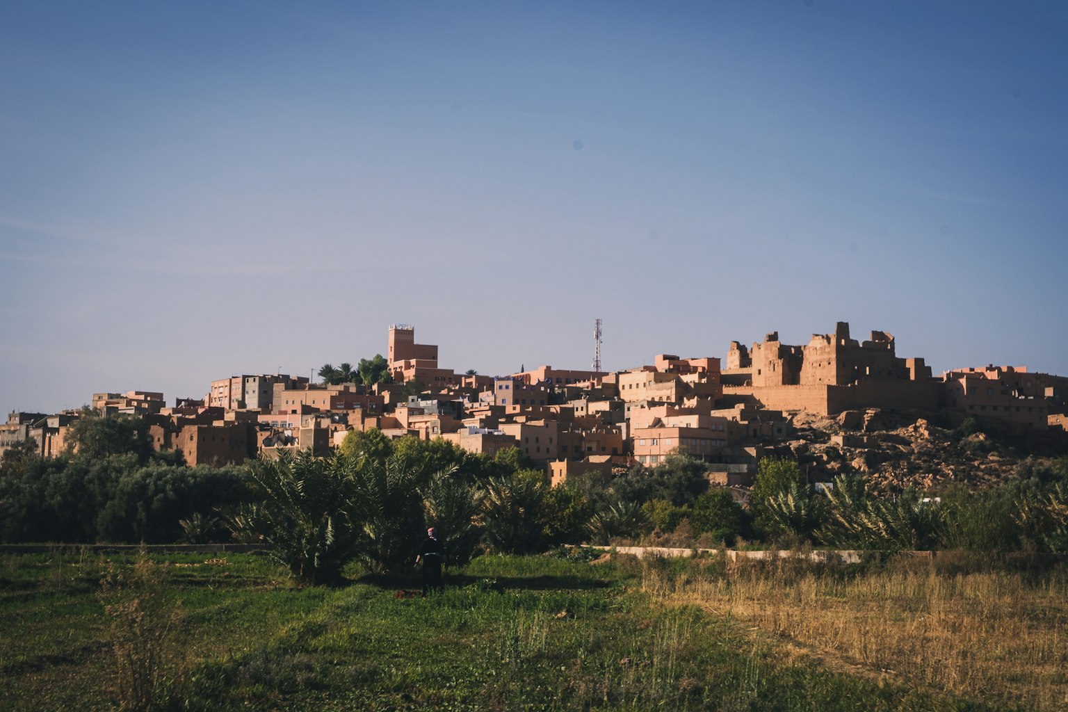 Una vista escénica de un antiguo pueblo bajo un cielo azul con hierba verde y edificios de tierra