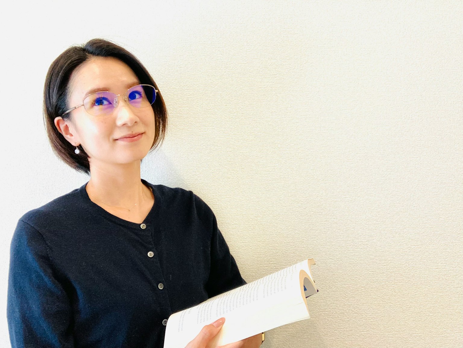 Donna che sorride mentre tiene un libro davanti a un muro bianco